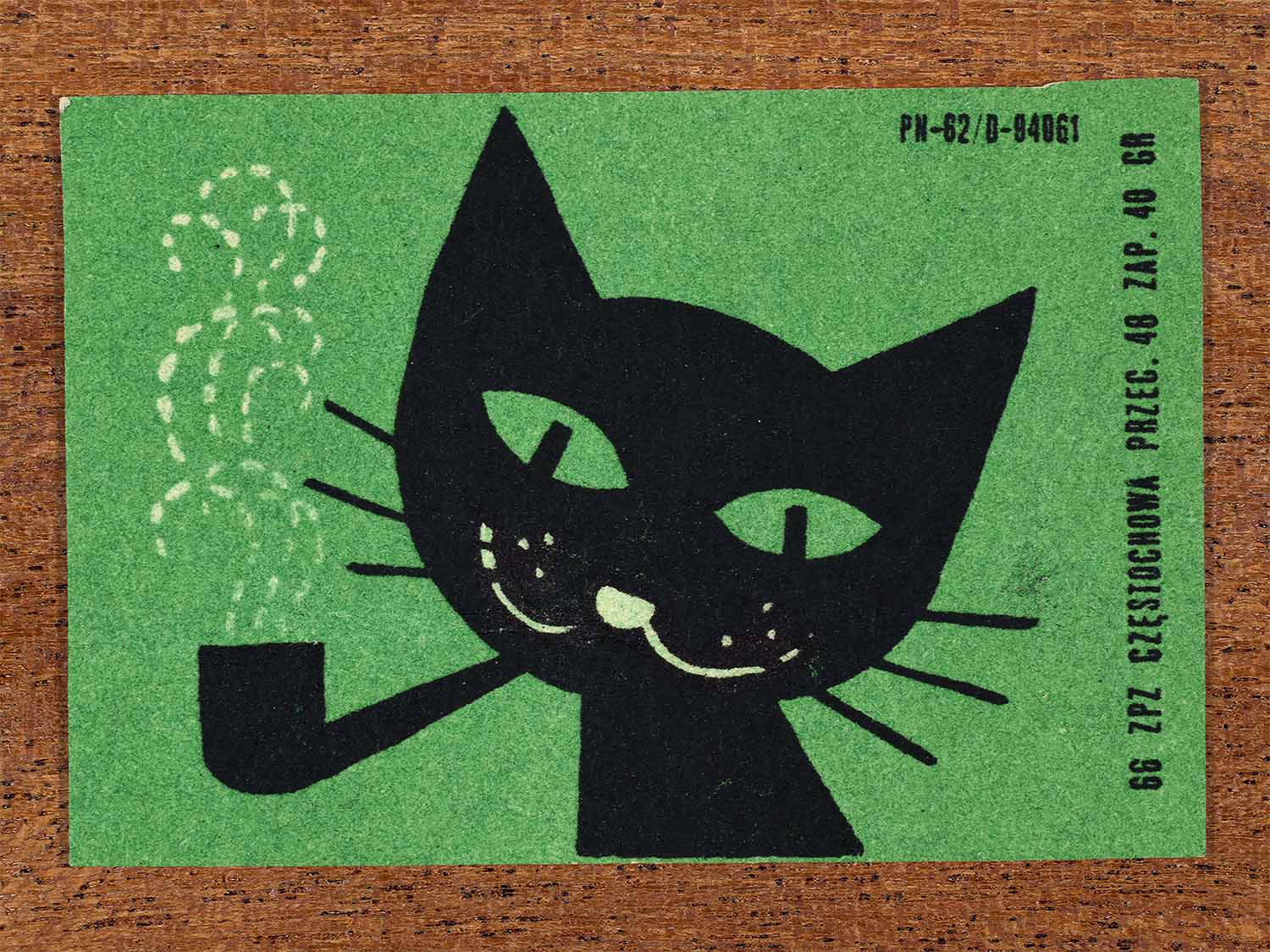 Vintage 1966 Polish matchbox label showing a stylised black cat smoking a pipe with white dotted smoke on a green background. Produced by the Częstochowa match factory in Poland as retail packaging for safety matches.