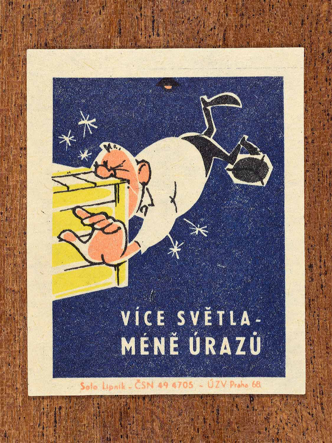 Vintage 1968 Czech matchbox label featuring a cartoon person tripping and falling nose-first into a big yellow box, on blue background. Produced by Solo Lipník match factory to promote proper lighting and maintenance for eye health and safe work practices.