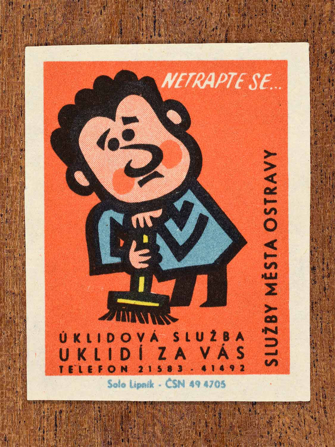 Vintage 1967 Czech matchbox label showing a cartoon man frowning while sweeping with a broom, on a red background. Produced by the Solo Lipník match factory to promote municipal home cleaning services.