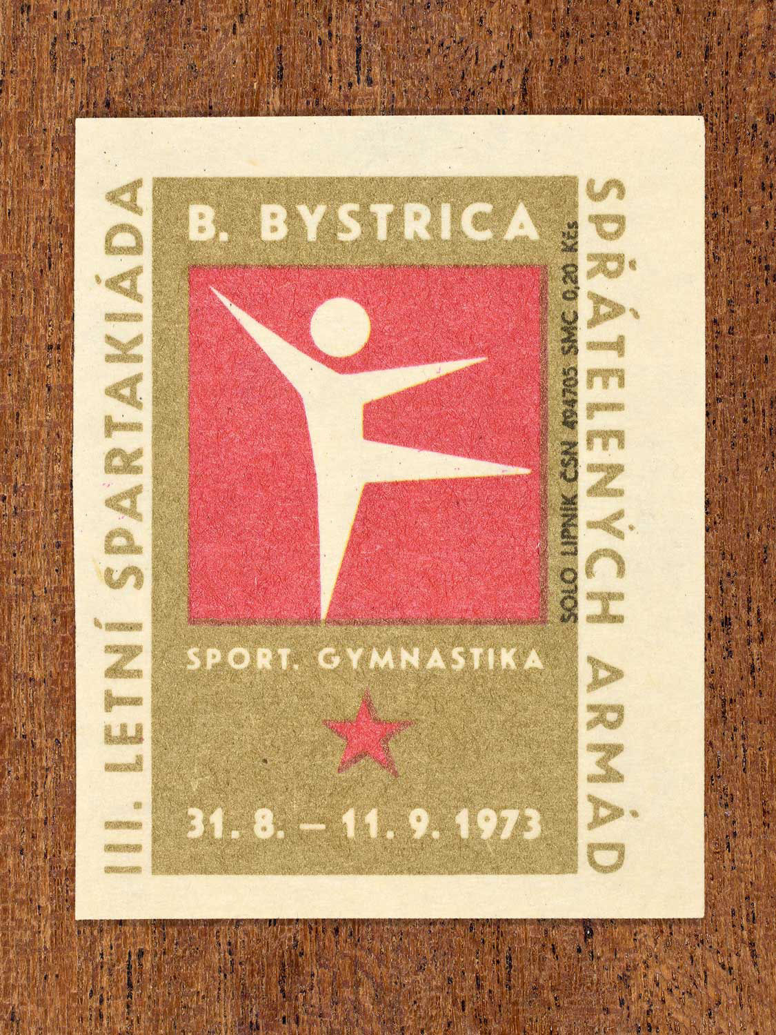 Vintage 1973 Czech matchbox label showing a simplified white gymnast figure on a red and gold background. Produced by the Solo Lipník match factory to promote physical training and demonstrate collective military readiness among allied armies.