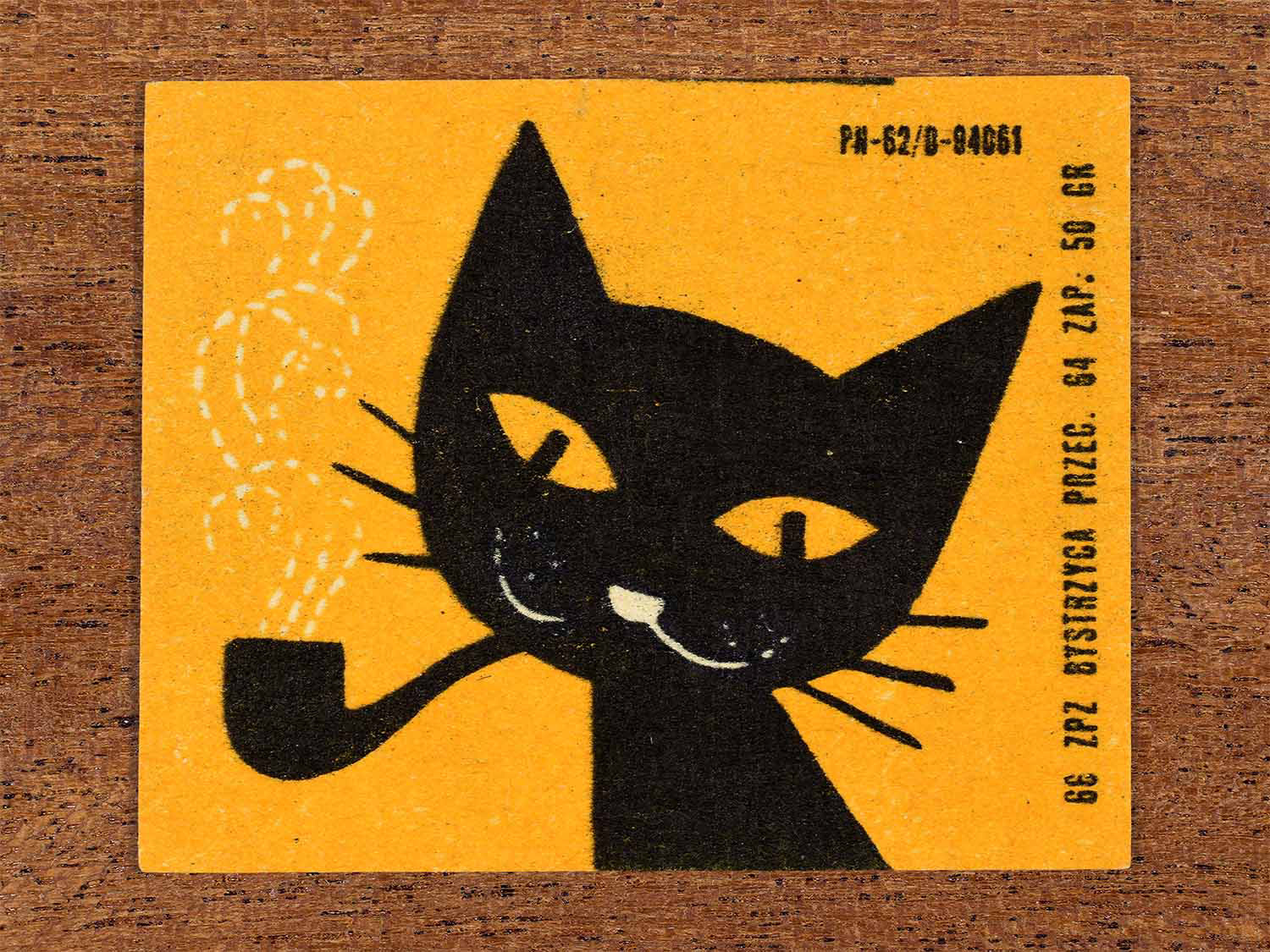Vintage 1966 Polish matchbox label showing a stylised black cat smoking a pipe with white dotted smoke on an orange background. Produced by the Bystrzyca match factory in Poland as retail packaging for safety matches.
