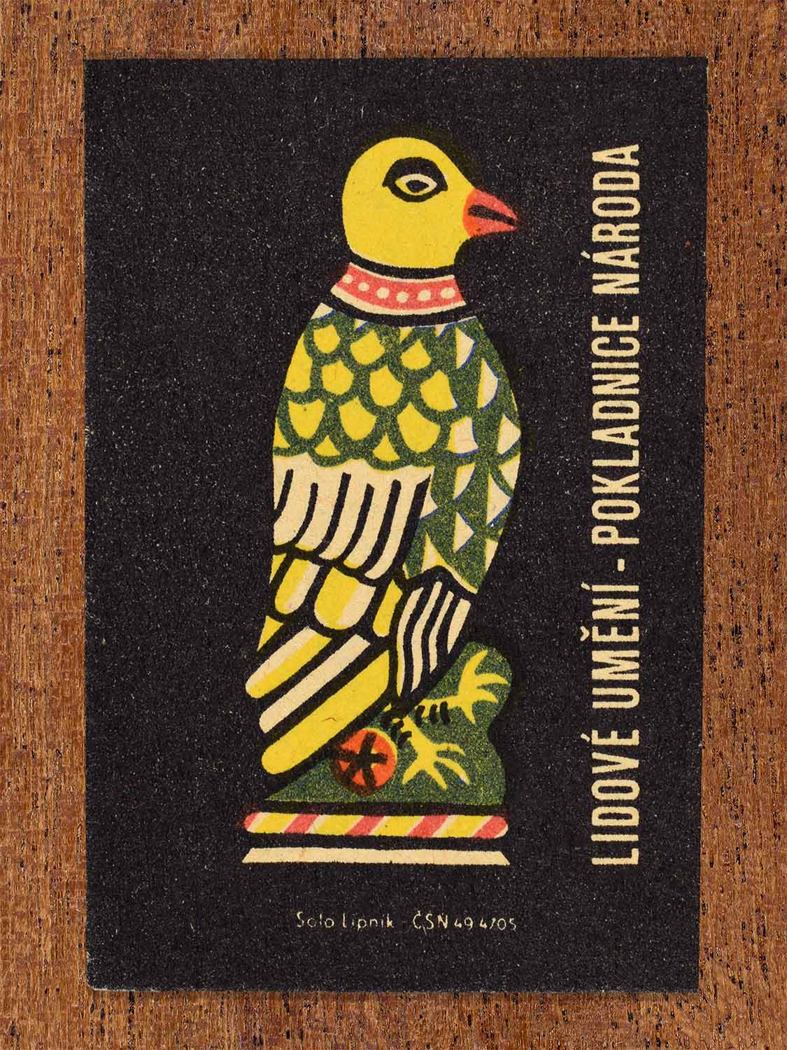 Vintage c. 1962 Czech matchbox label showing a stylised folk bird sculpture with patterned plumage in yellow and green tones. Produced by the Solo Lipník match factory to showcase traditional decorative folk motifs