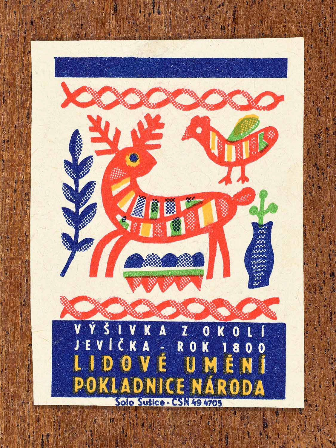 Vintage 1964 Czech matchbox label showing a stylised deer and bird rendered as folk patterns in bright red, blue and green. Produced by the Solo Sušice match factory to highlight traditional regional embroidery from the Jevíčko area.