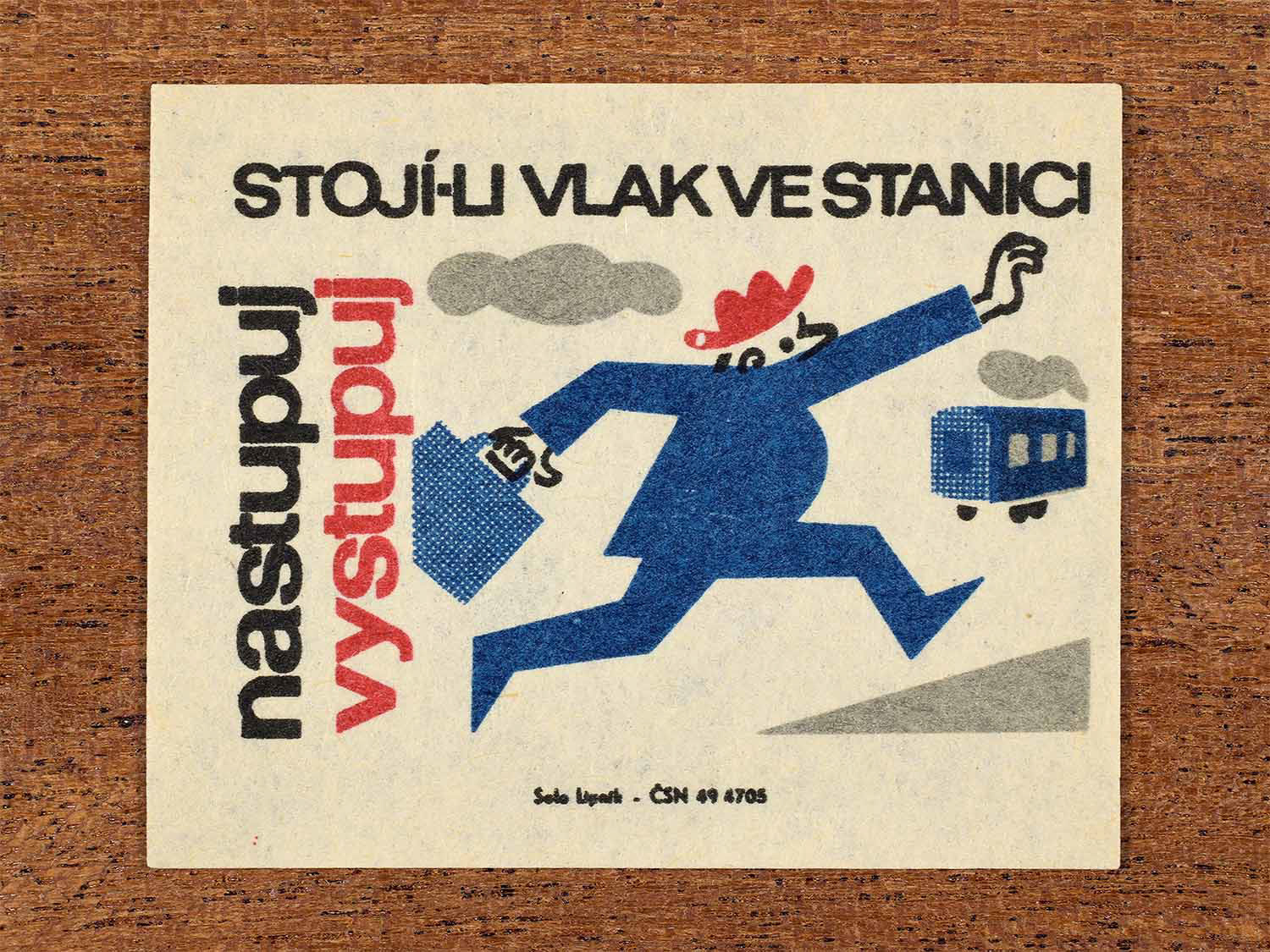 Vintage c. 1964 Czech matchbox label showing a man running after a moving train, illustrated in blue, red and black. Produced by the Solo Lipník match factory to warn passengers to board and disembark only when trains are stopped.