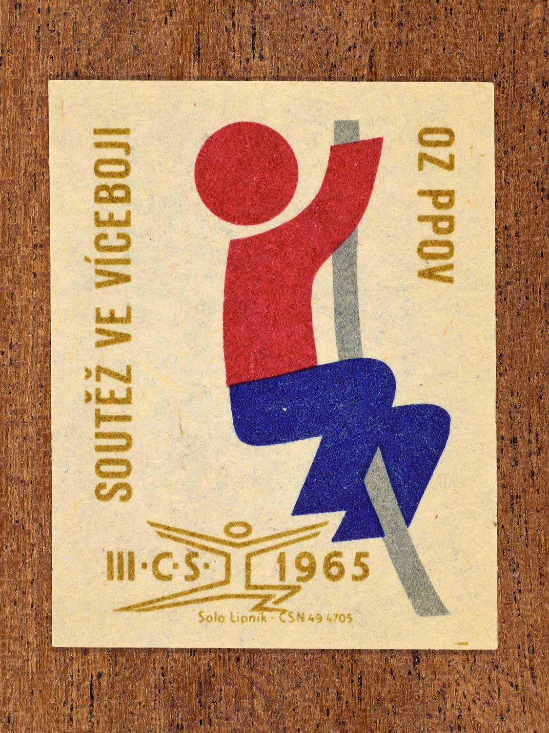 Vintage 1965 Czechoslovak matchbox label showing an abstract athlete figure, in blue, red and gold colours. Produced by the Solo Lipník match factory to promote physical fitness and sporting achievement.