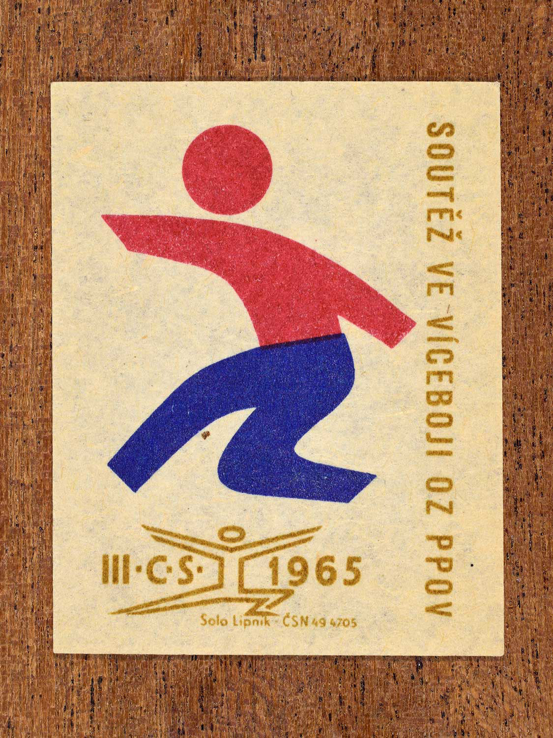 Vintage 1965 Czechoslovak matchbox label showing an abstract athlete figure, in blue, red and gold colours. Produced by the Solo Lipník match factory to promote physical fitness and sporting achievement.