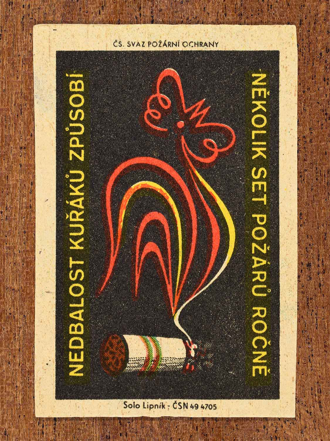 Vintage c. 1961 Czech matchbox label showing a stylised rooster formed from cigarette smoke rising from a lit cigarette, in black, red and yellow colours. Produced by the Solo Lipník match factory to warn that careless smoking causes hundreds of fires annually.
