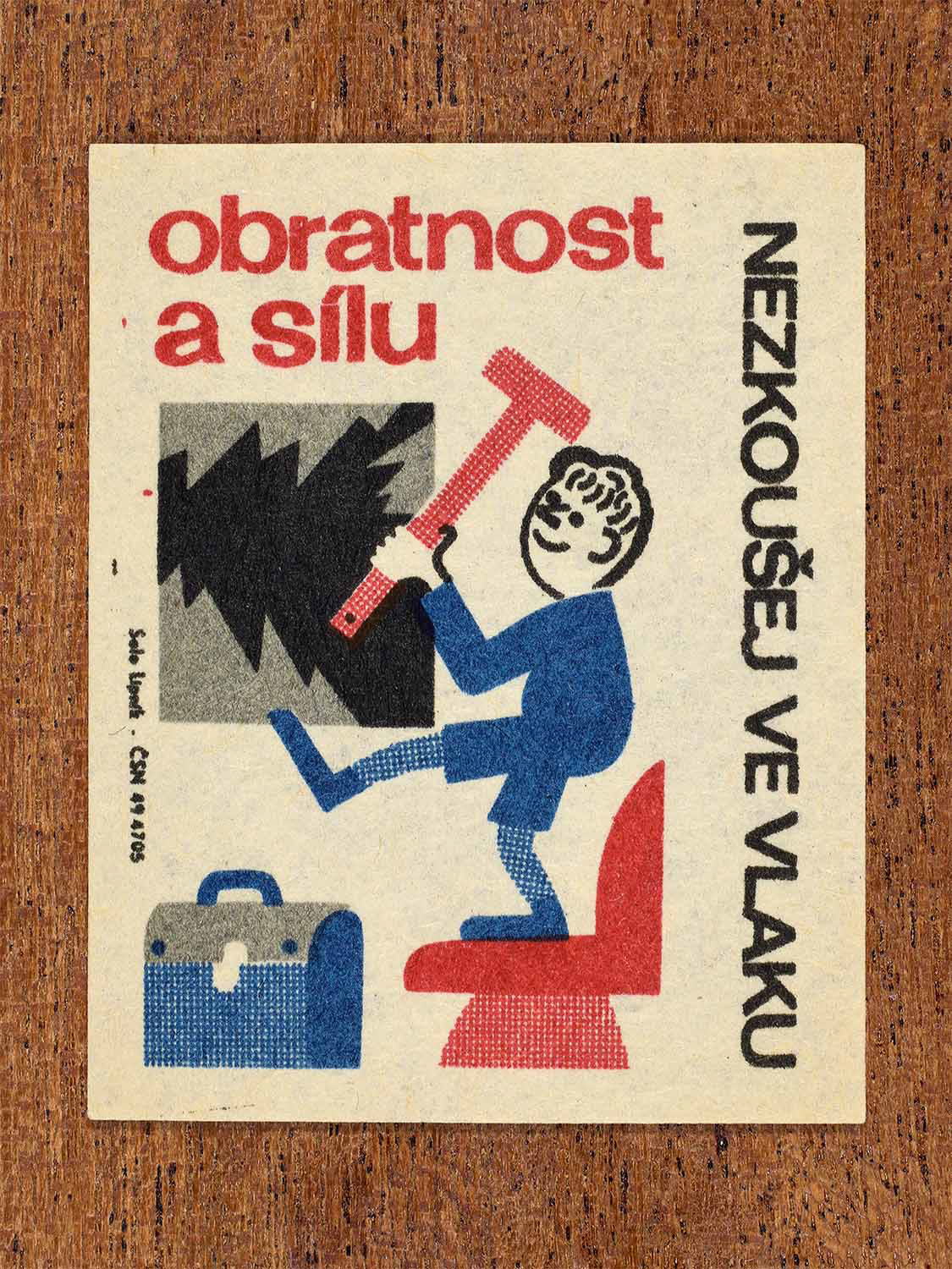 Vintage c. 1964 Czech matchbox label showing a man swinging a hammer inside a train carriage, illustrated in red, blue and black. Produced by the Solo Lipník match factory to warn against dangerous behaviour on trains.