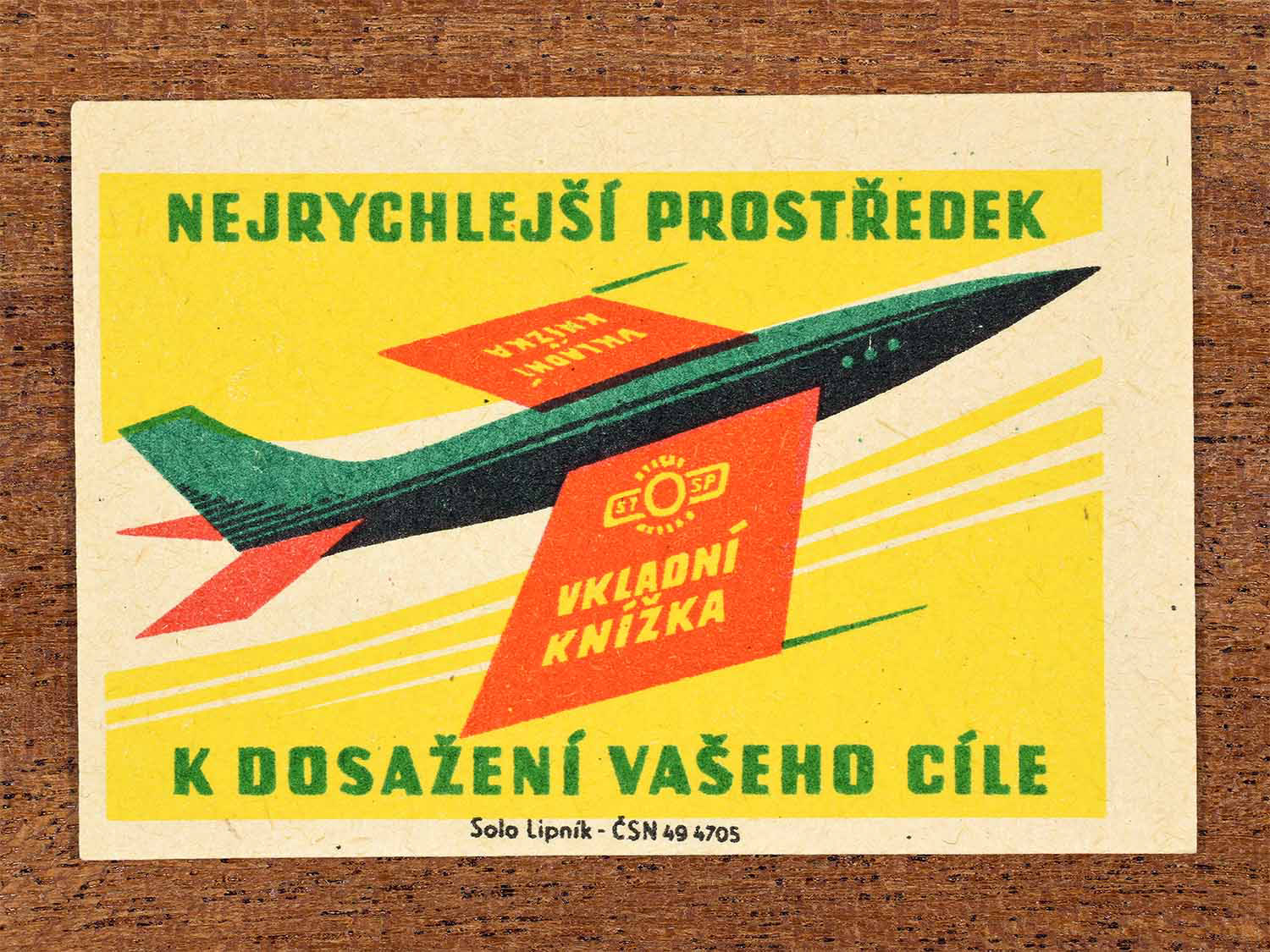 Vintage 1960 Czech matchbox label showing a flying aeroplane with pages of a savings book for wings, in bright colours. Produced by the Solo Lipník match factory to promote saving through a passbook to achieve long-term goals.