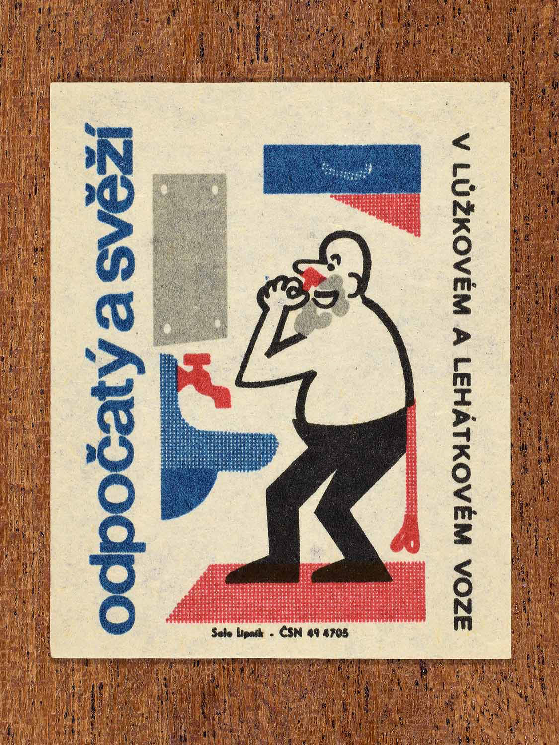Vintage c. 1964 Czech matchbox label showing a passenger shaving at a wash area, illustrated in blue, red and black. Produced by the Solo Lipník match factory to promote resting and sleeping in couchette train carriages.