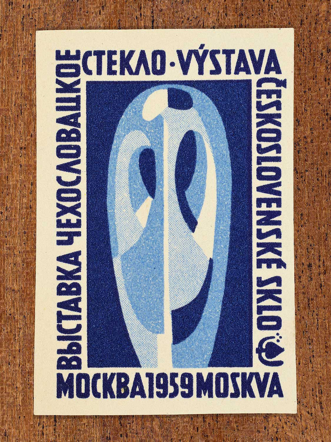 Illustration of an oval glass ornament on a blue background depicted on a vintage 1959 Czechoslovak matchbox label. Produced by an unknown factory to promote mid-century abstract sculptural trends in glass art at international glass exhibition in Moscow.