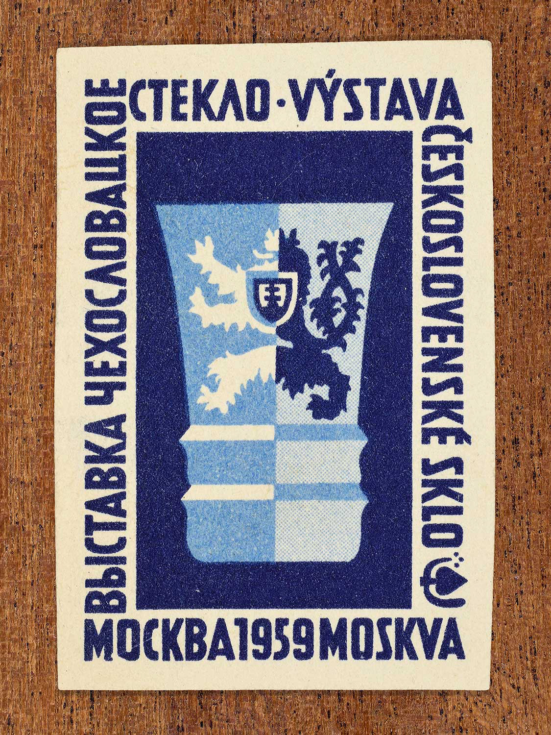 An illustration of a stylised glass vessel on a blue backdrop depicted on a matchbox label. The design functions to celebrate the artistry of Czechoslovak glass craftsmanship as exhibited at an event in Moscow, 1959.