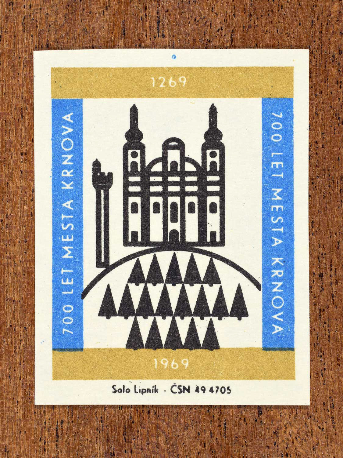 Vintage 1969 Czech matchbox label showing the Pilgrimage Church of Our Lady of Sorrows on Cvilín Hill above Krnov, in black, blue and gold. Produced by the Solo Lipník match factory to commemorate 700 years of the city of Krnov.