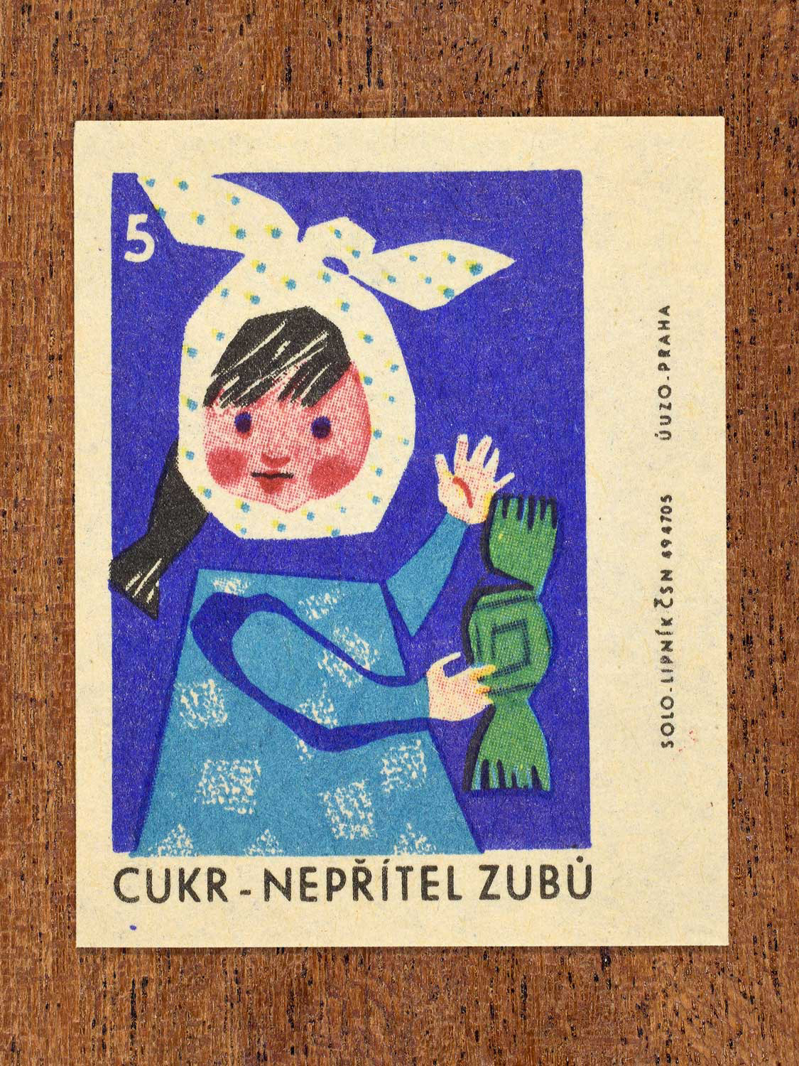 Vintage c. 1965 Czech matchbox label showing a child with a head bandage holding a large green wrapped sweet. Produced by Solo Lipník match factory to promote the health benefits proper nutrition, daily meal routines, and everyday household habits.