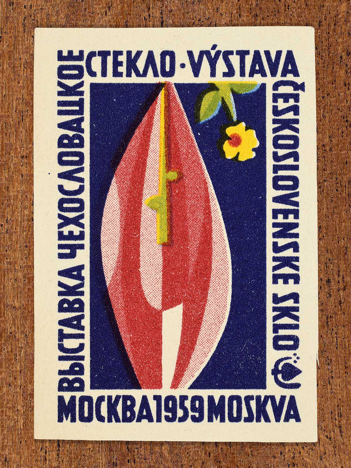 A mid-century illustration of a red glass sculpture on a blue background depicted on a 1959 vintage matchbox label. The design functions to promote an international Czechoslovak glass exhibition in Moscow.