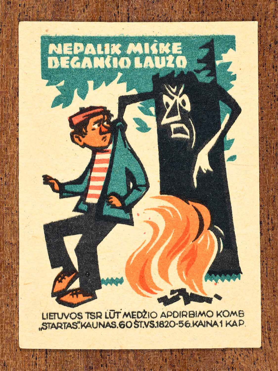 intage 1964 Lithuanian matchbox label showing a man leaving a burning campfire beside a tree with a face and arms. In black, green and orange colours. Produced by the Startas match factory to promote responsible behaviour in forests.