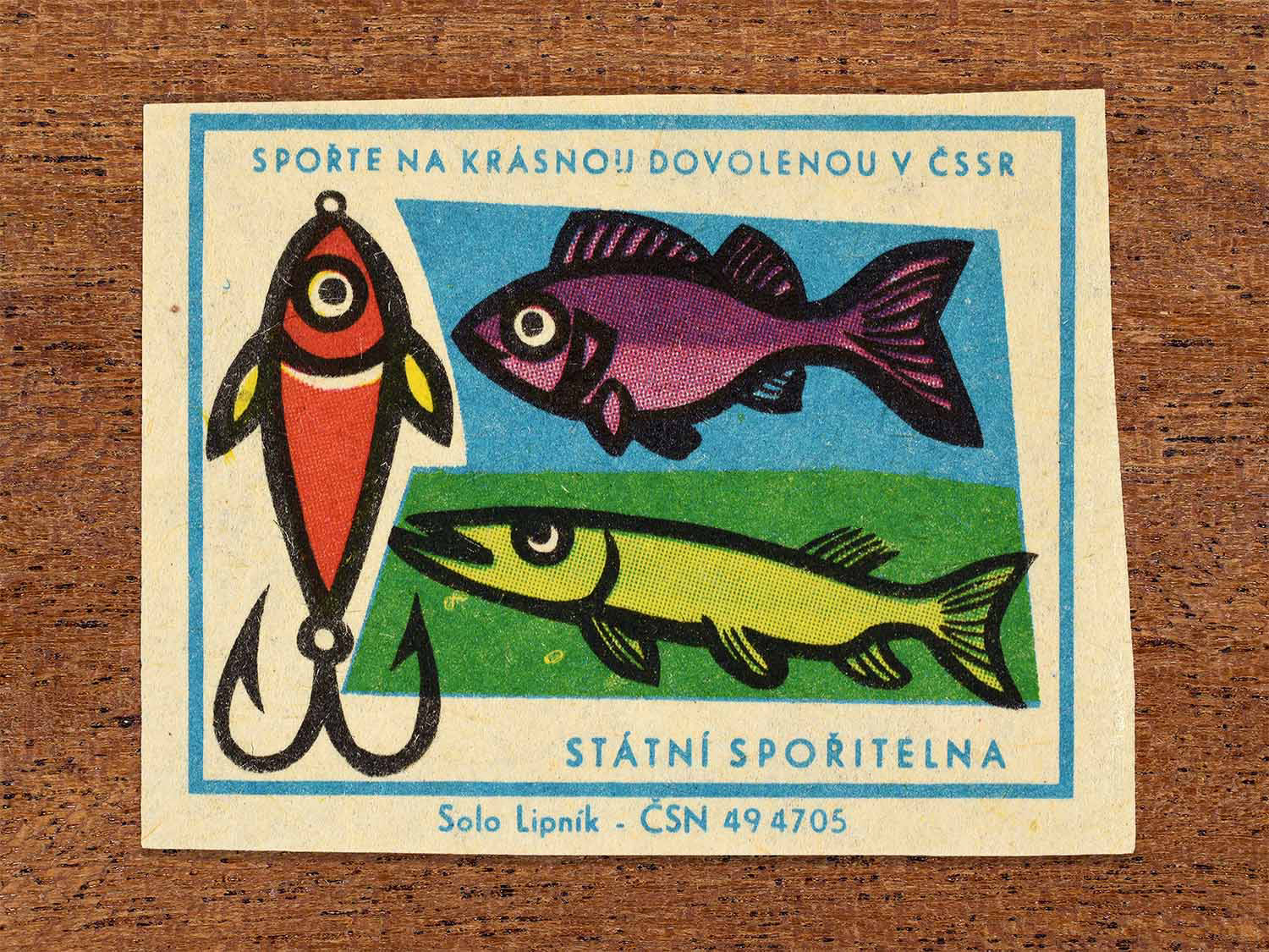 Vintage 1968 Czech matchbox label showing colourful fishing lures and stylised fish. Produced by the Solo Lipník match factory to promote saving money for holidays in the Czechoslovak Socialist Republic.