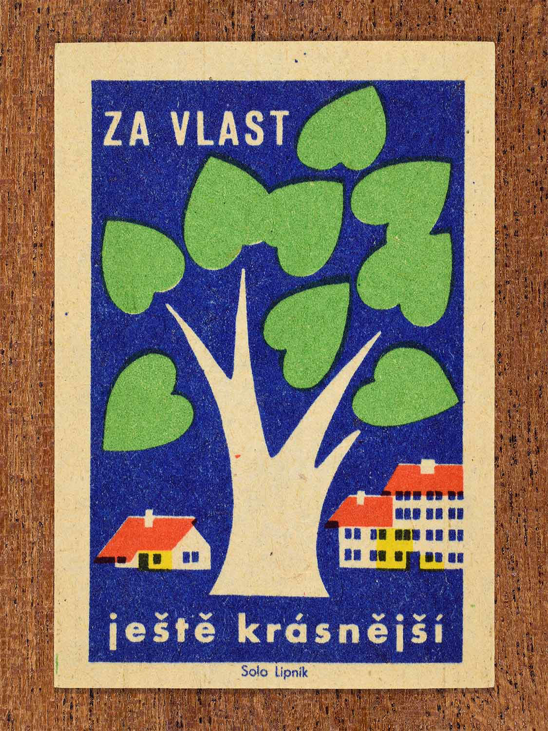 Vintage 1960 Czech matchbox label showing a large stylised white tree with green leaves beside houses and apartment buildings on a blue background. Produced by the Solo Lipník match factory to promote civic beautification and environmental.