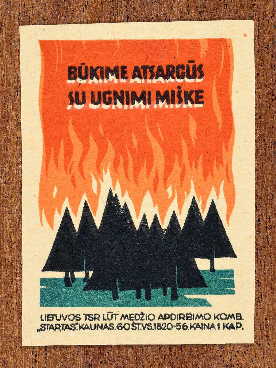 Vintage 1964 Lithuanian matchbox label showing a forest silhouette beneath a wall of flames. In black, green and orange colours. Produced by the Startas match factory to promote safe behaviour in woodland areas.
