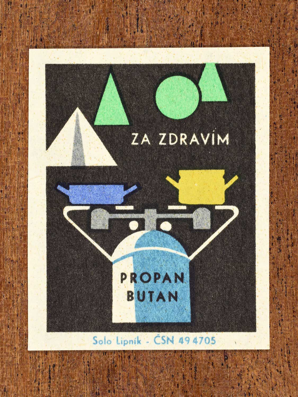 Vintage c. 1966 Czech matchbox label showing a portable gas heater and pots with a tent and trees behind. In green, blue, yellow and black colours. Produced by the Solo Lipník match factory to promote safe, modern, and responsible domestic propane–butane gas use.