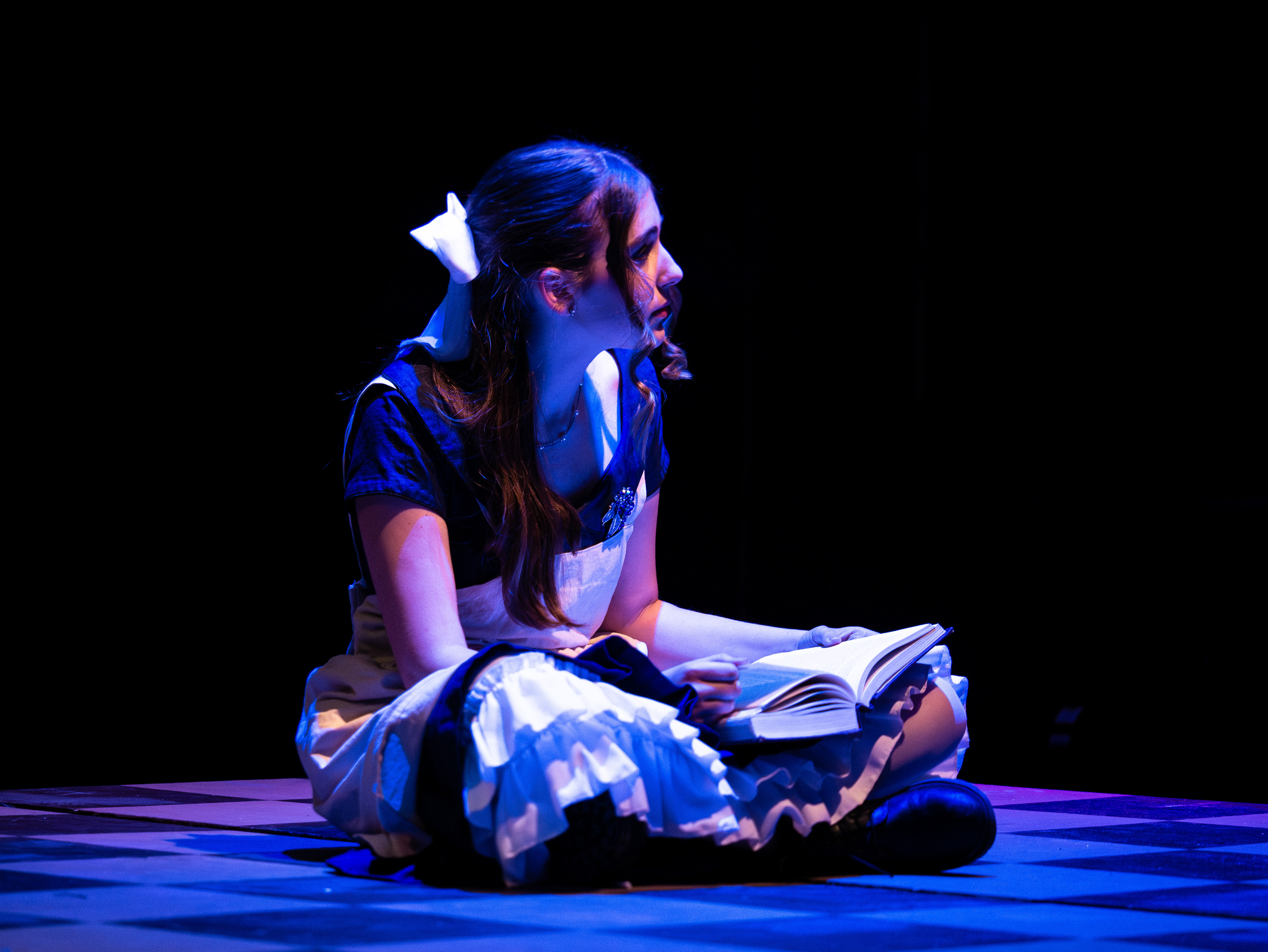 Sierra Little (Alice) sits onstage during the entire pre-show as audience members enter the black box