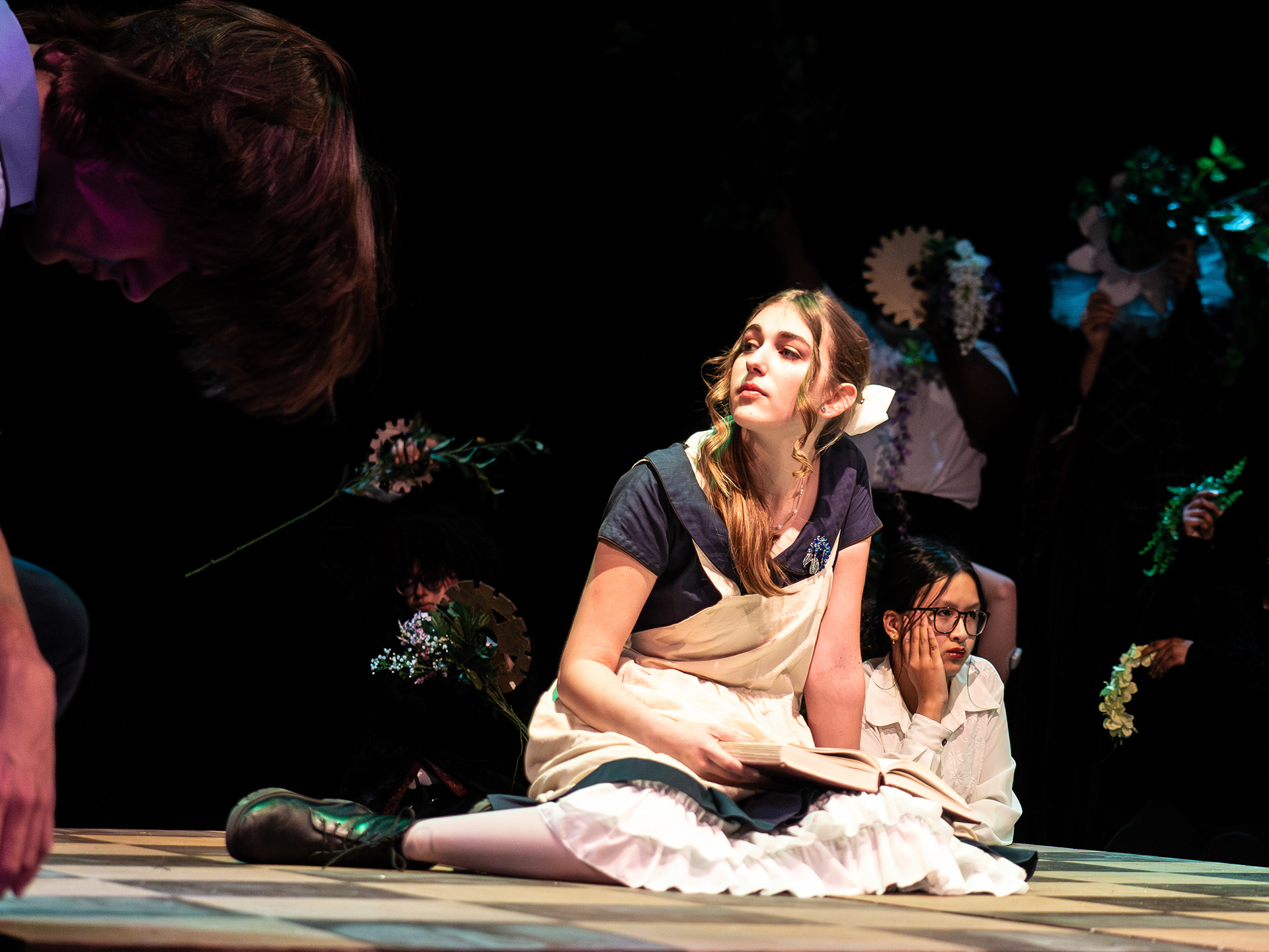 Ensemble members holding flowers and gears stimulate Alice's descent into Wonderland