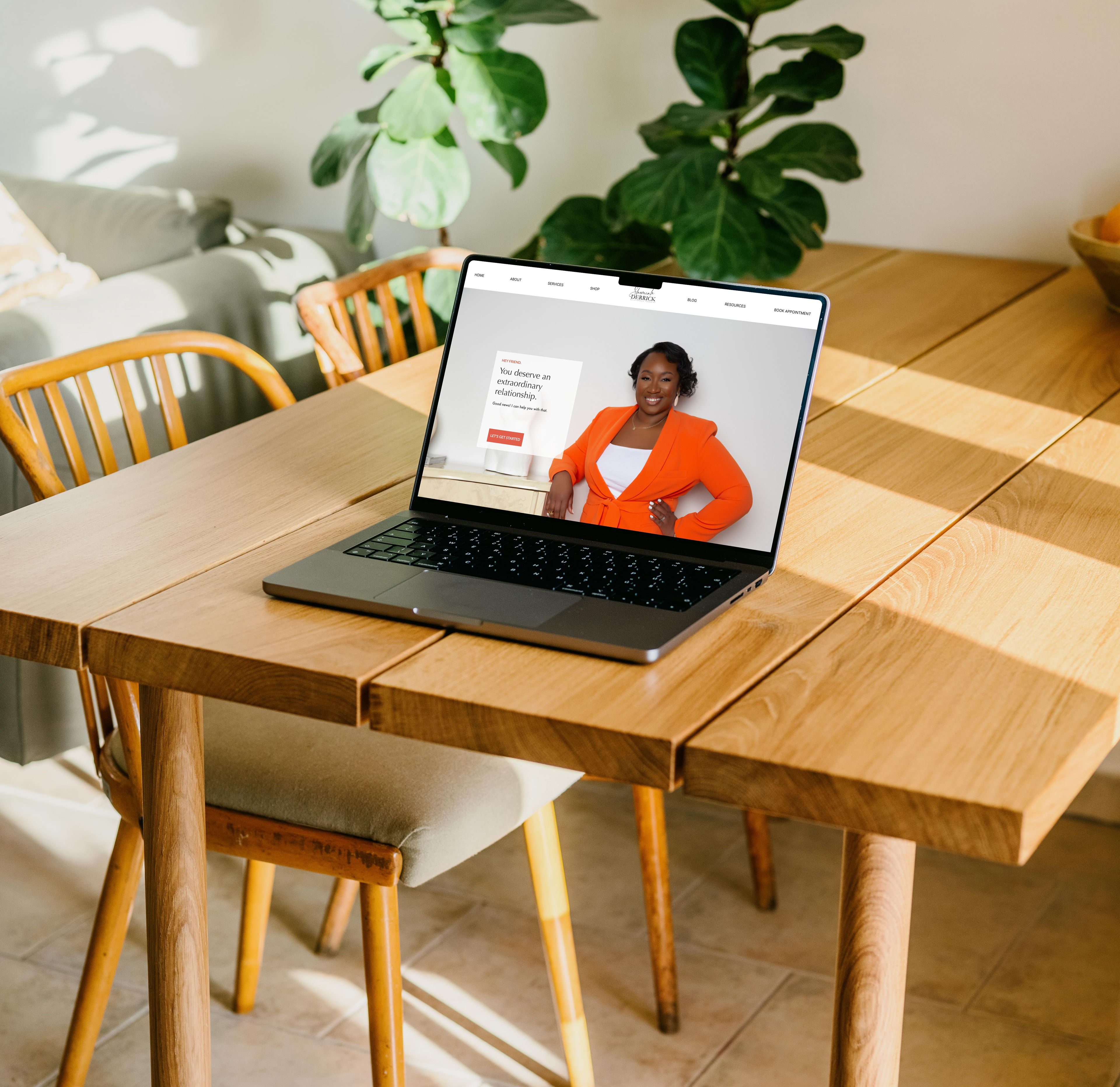 A MacBook Pro on a wooden table displays website homepage.