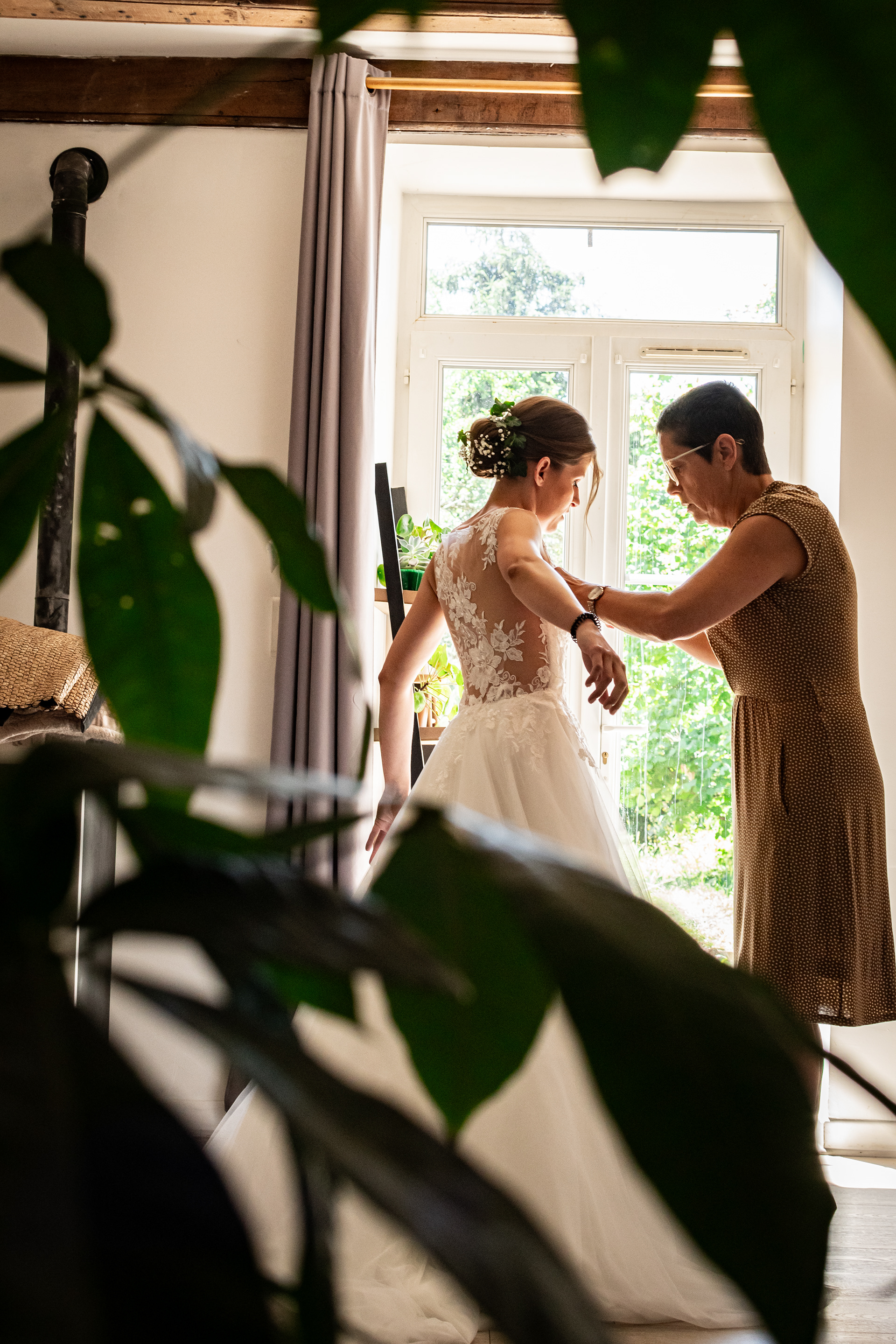 La mariée aidée par sa maman pour revêtir la précieuse robe blanche