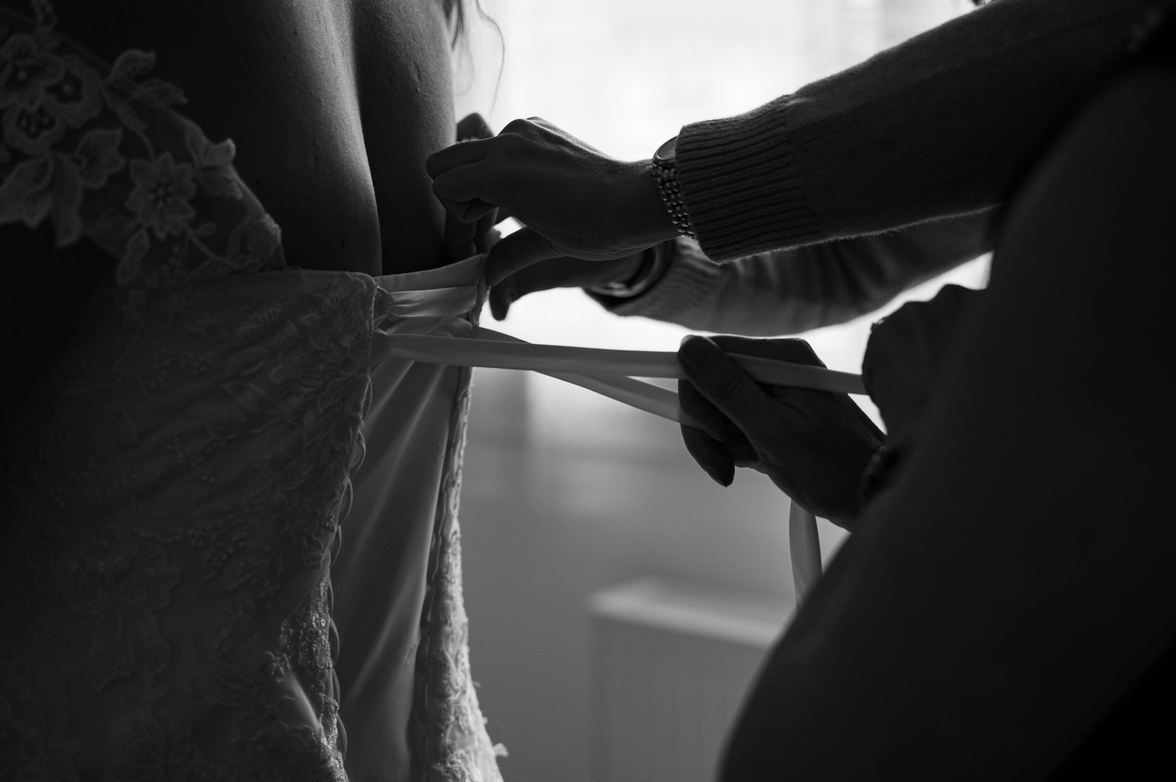 la mère de la mariée et sa témoin lacent ensemble la robe de la mairée