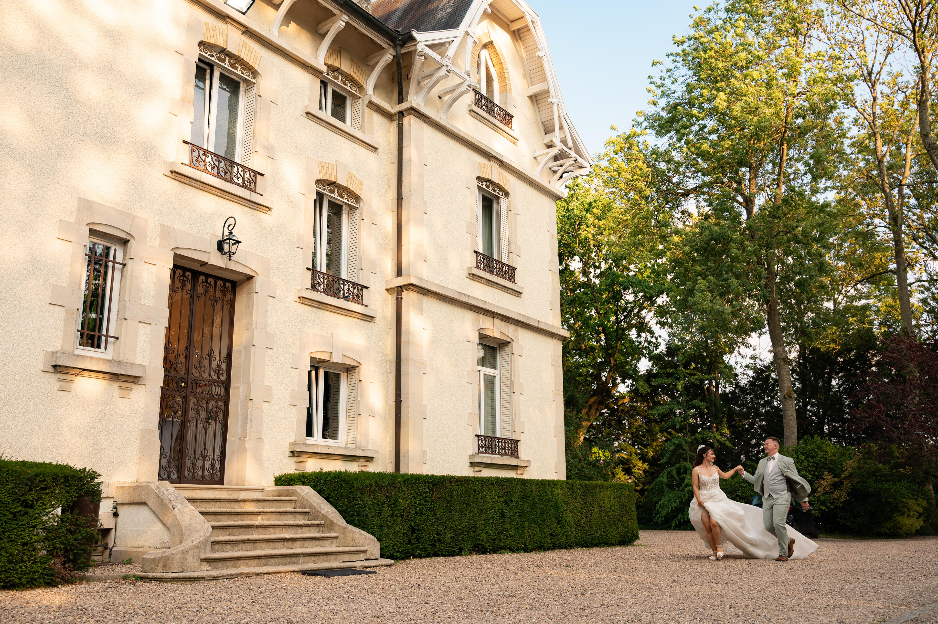 Couple de mariés courant devant un élégant domaine lors de leur mariage en Lorraine.