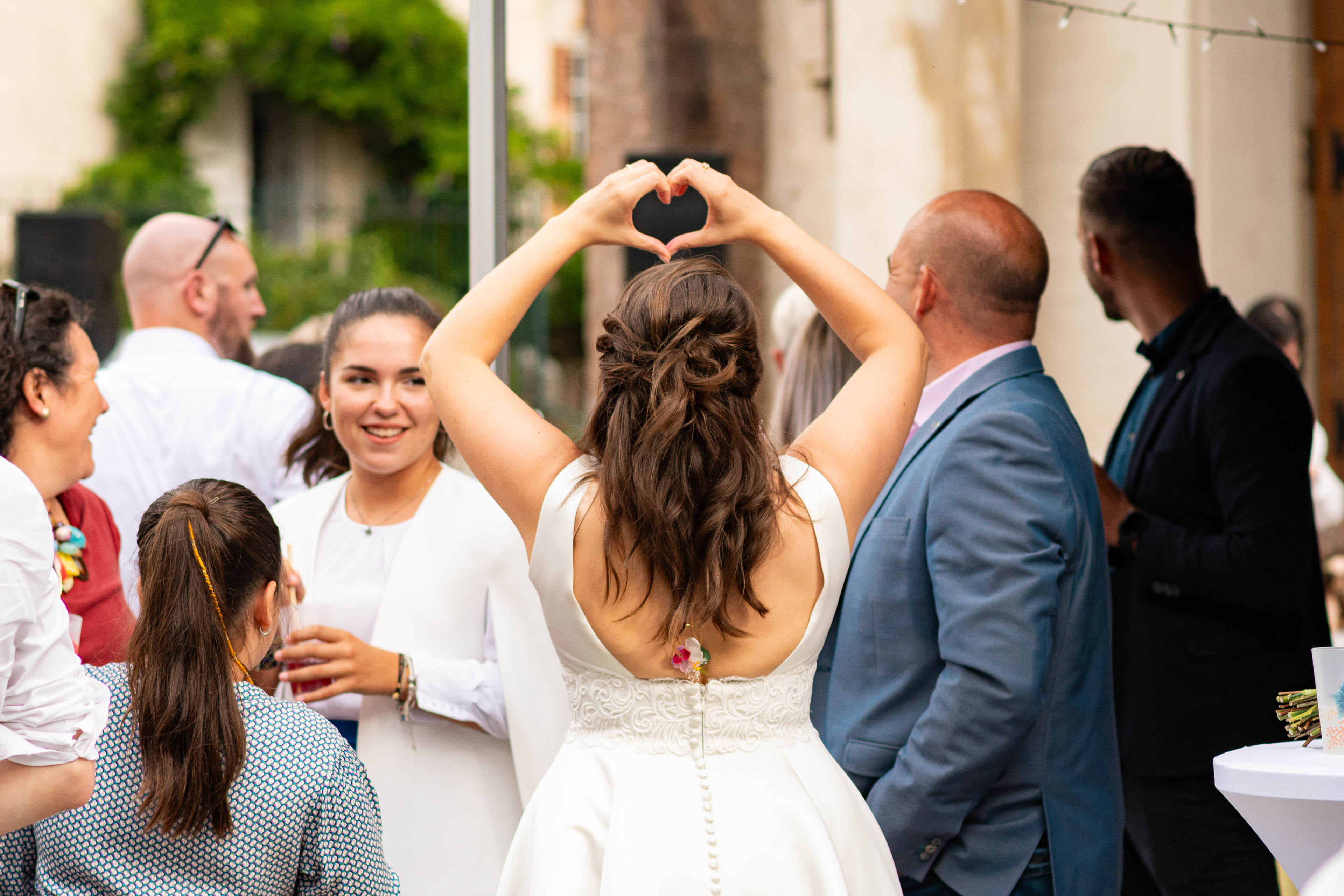 photos prise sur le vif par lilidep photo d'une mariée envoyant un cœur avec les mains à son mari pendant le vin d'honneur