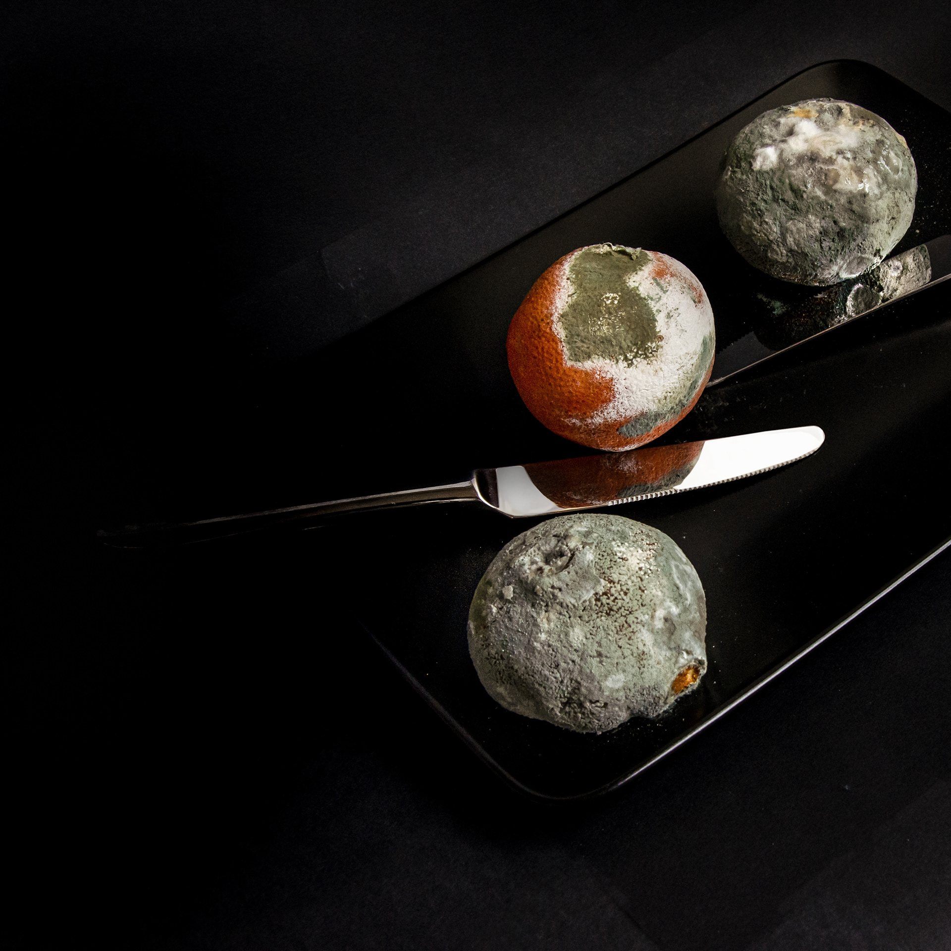 cut mouldy citrus with knife on dark background