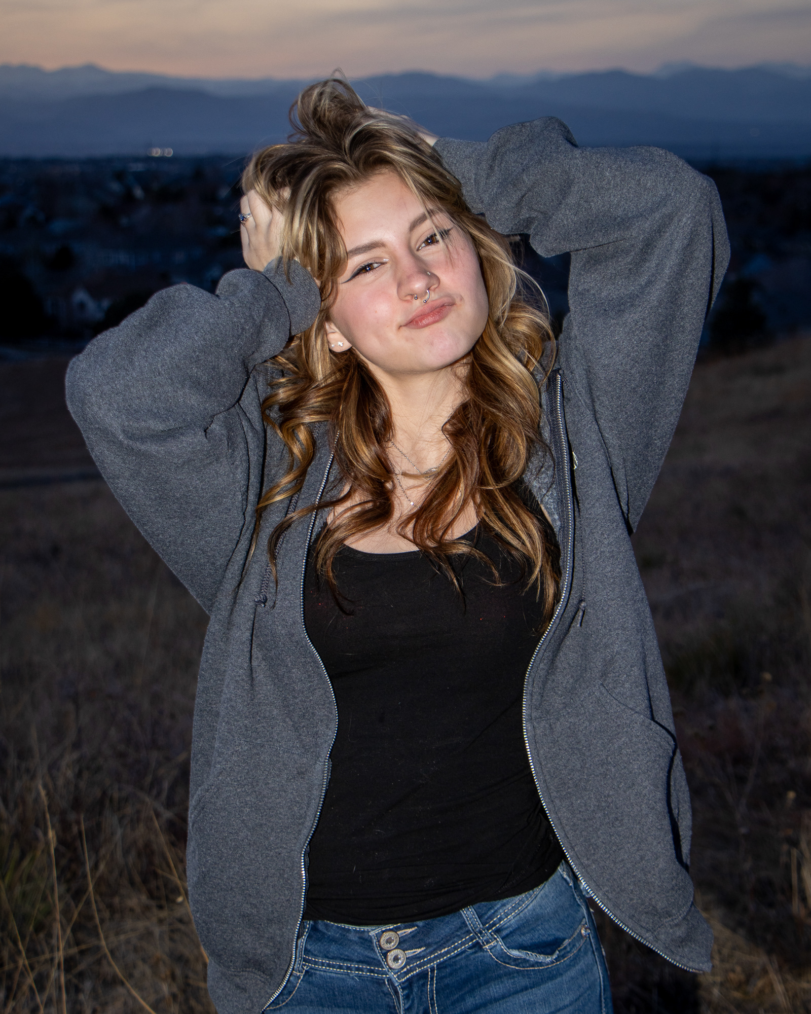 Woman smiling with hands in her hair, scenic background at dusk