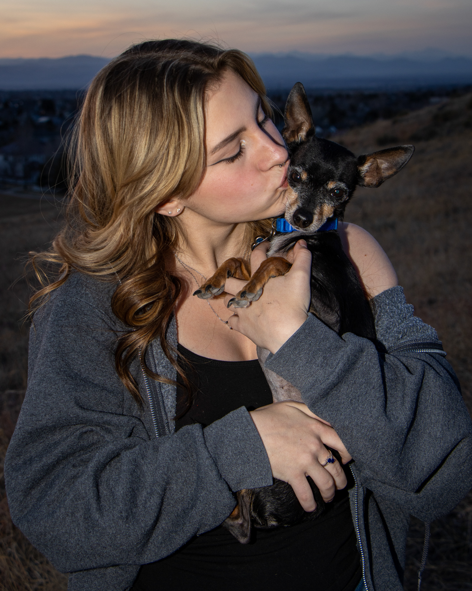 Woman kissing a small, black chihuahua on the face