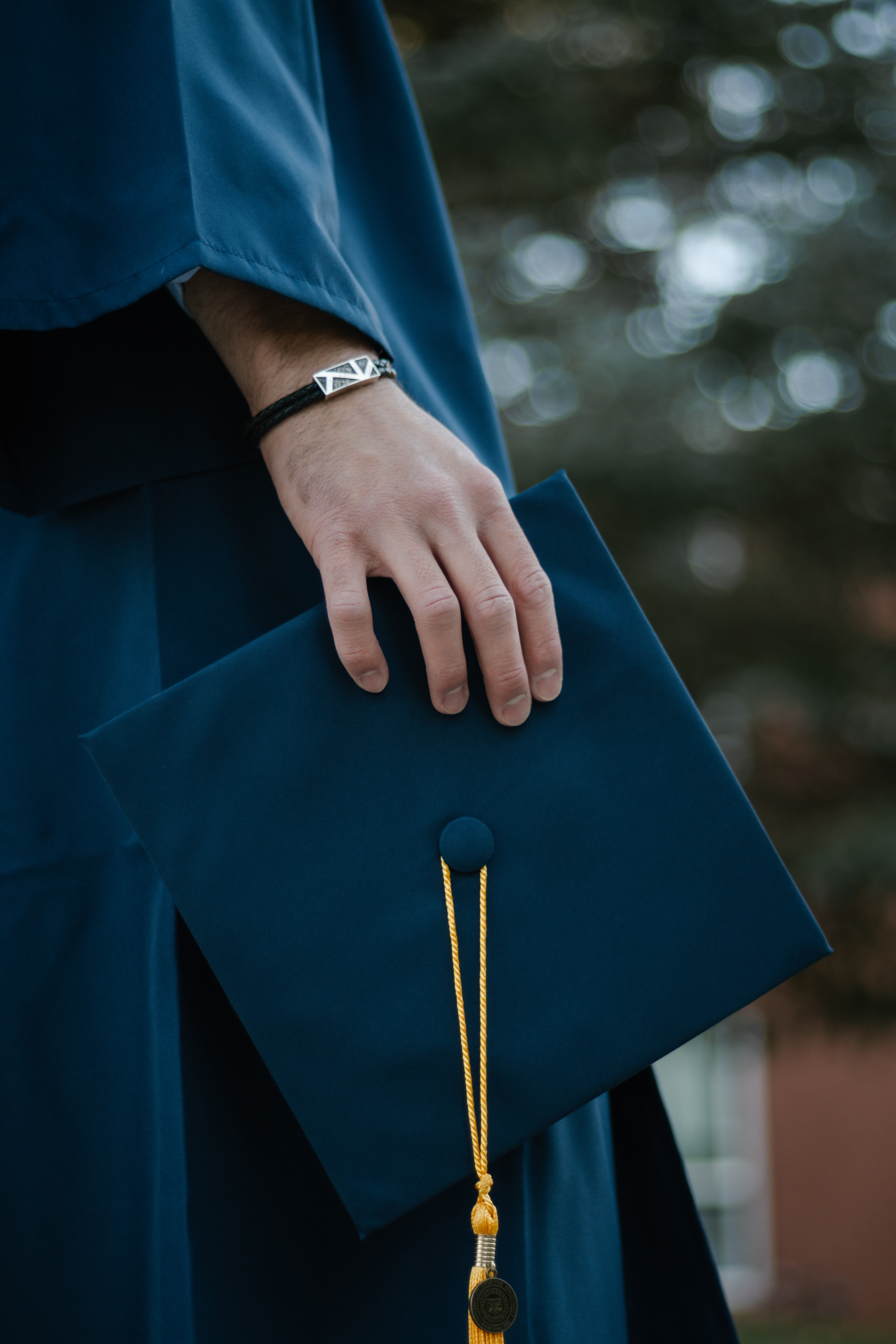 Close-up of a man's hand holding a graduation cap with a tassel on it