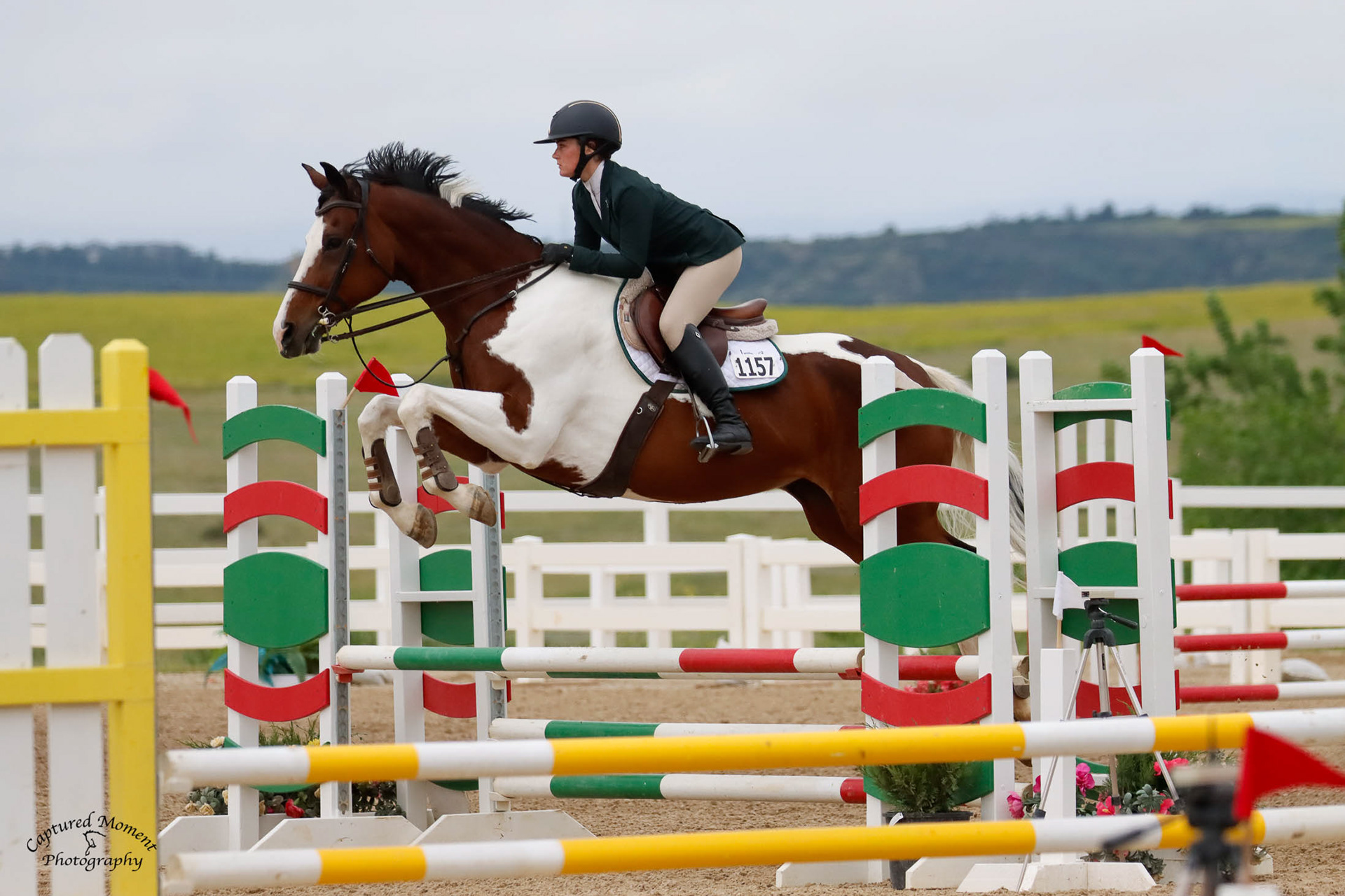 Rider and paint horse leaping ocer a green and red oxer