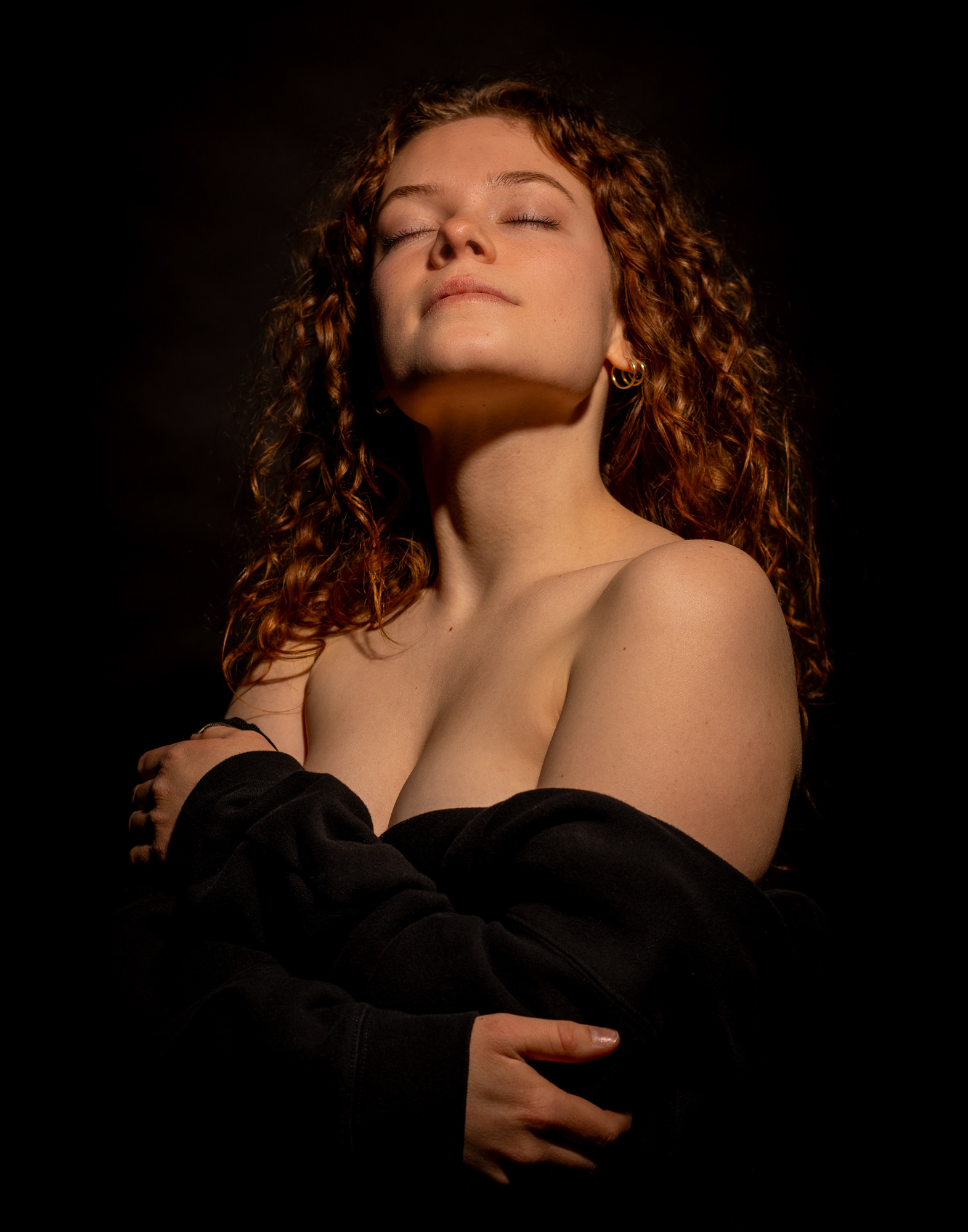 Woman with curly hair posing in soft, warm light with an off-shoulder top