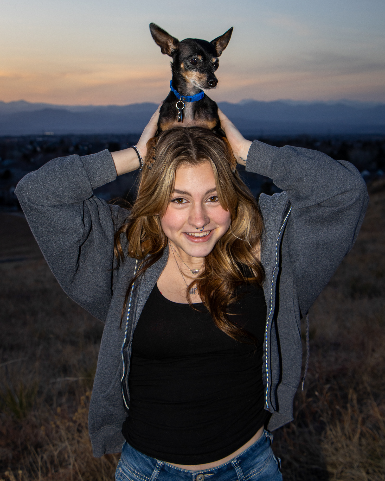 Woman holding a small black chihuahua on her head with a playful expression