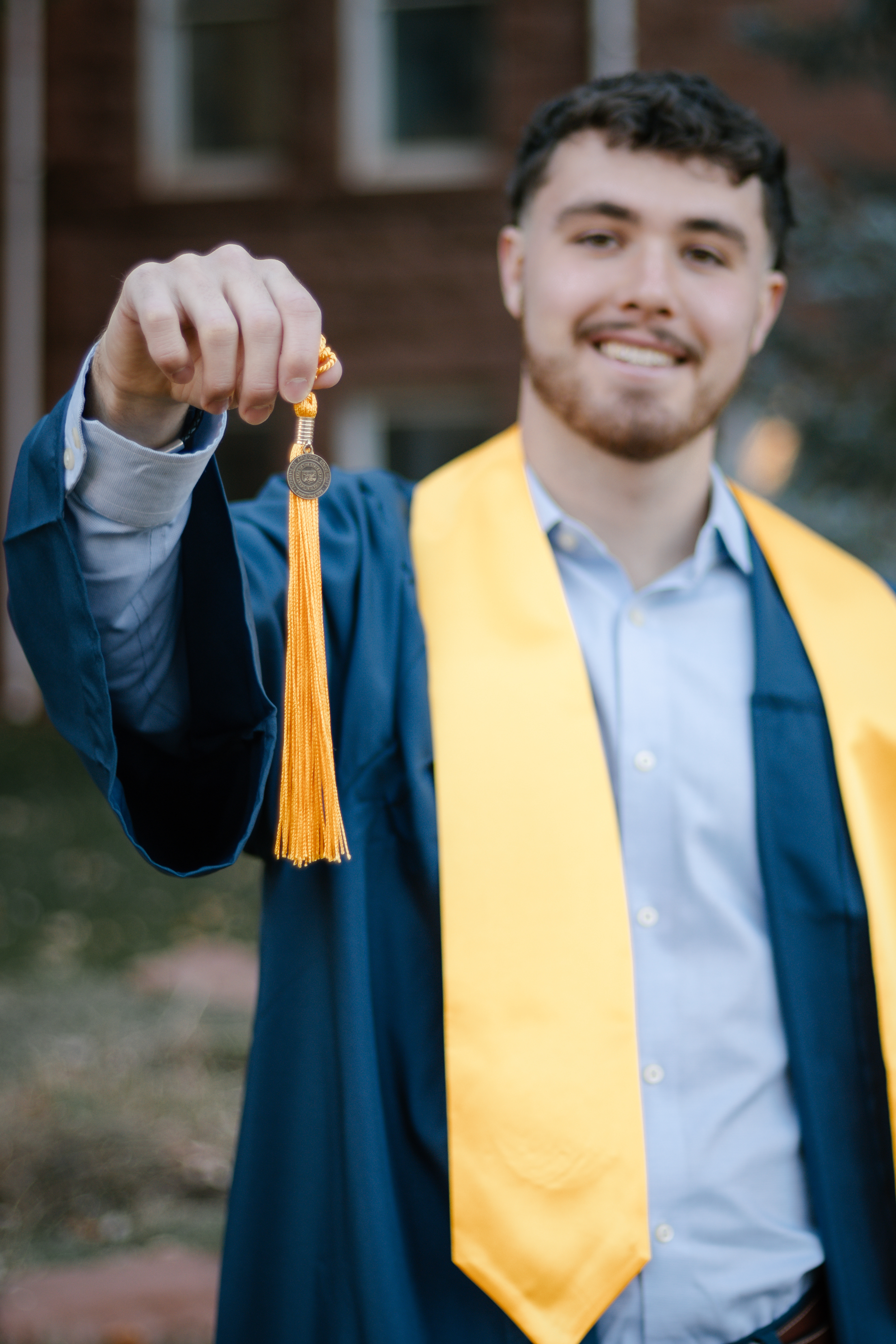 Man in grafuation down and yellow stole holding up his tassel