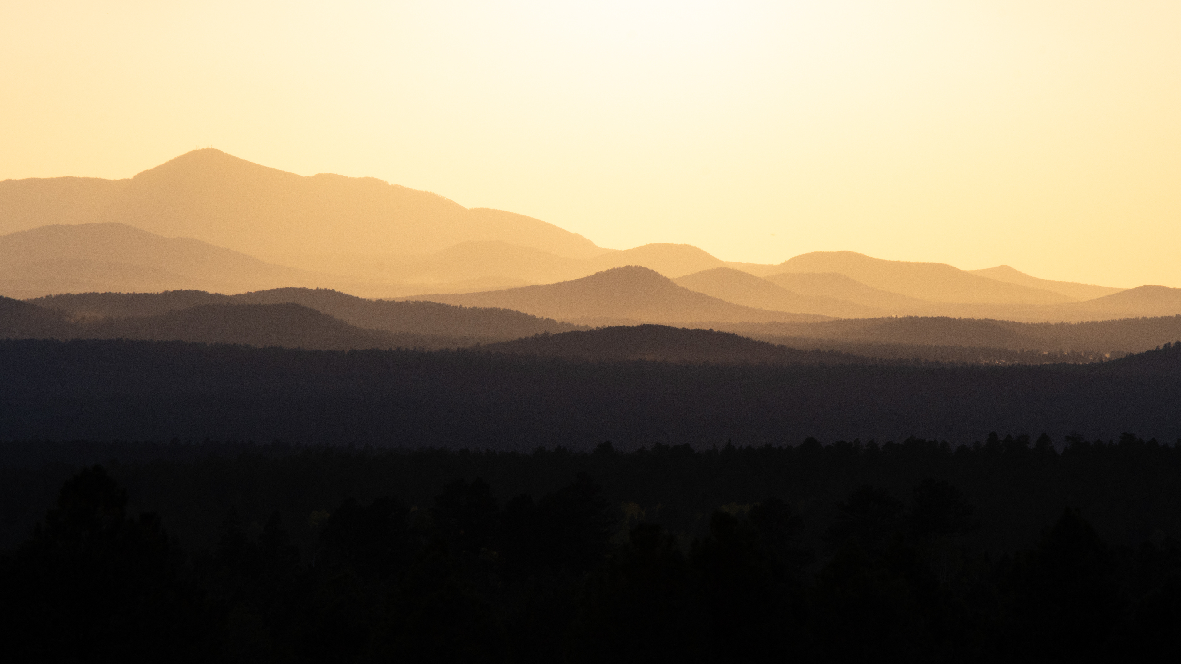 Layers of hazy mountain ridges at sunset with soft cool, and golden tones