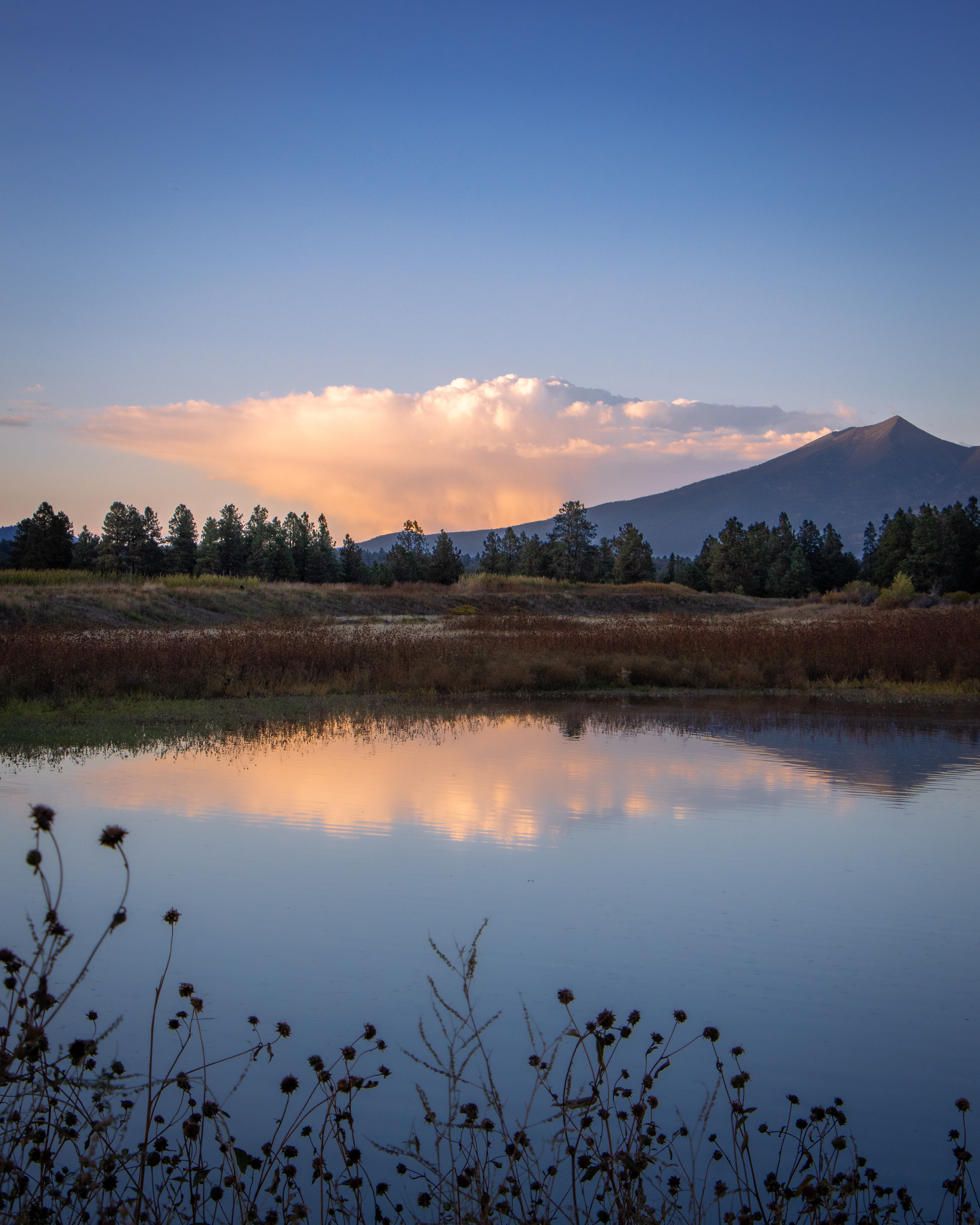 Calm lake reflecting distant mountains and soft evening sky