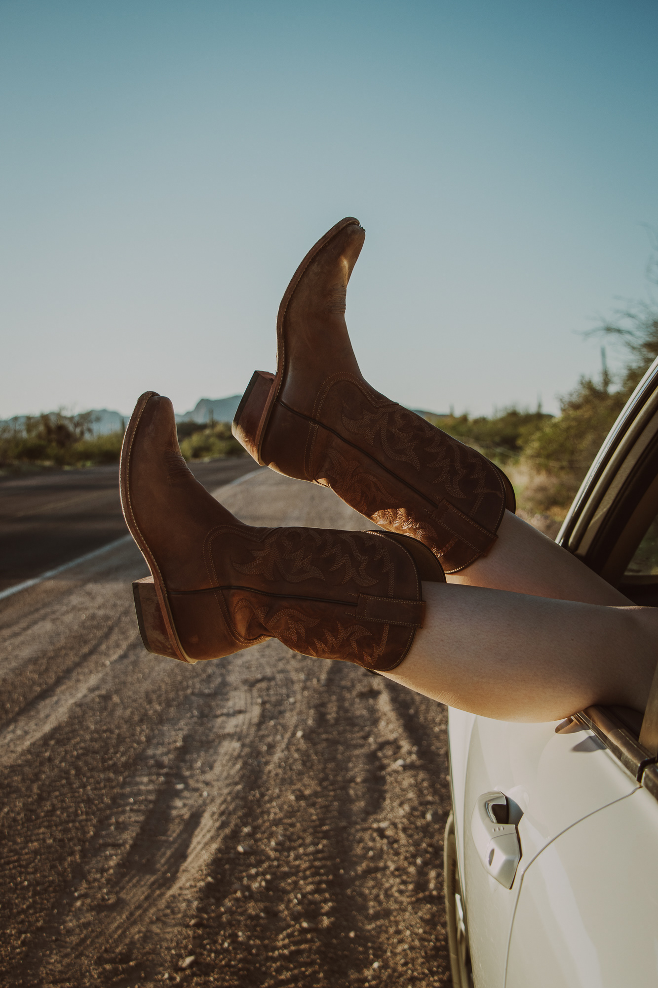 Close-up of cowboy boots hanging out of a car window at sunset