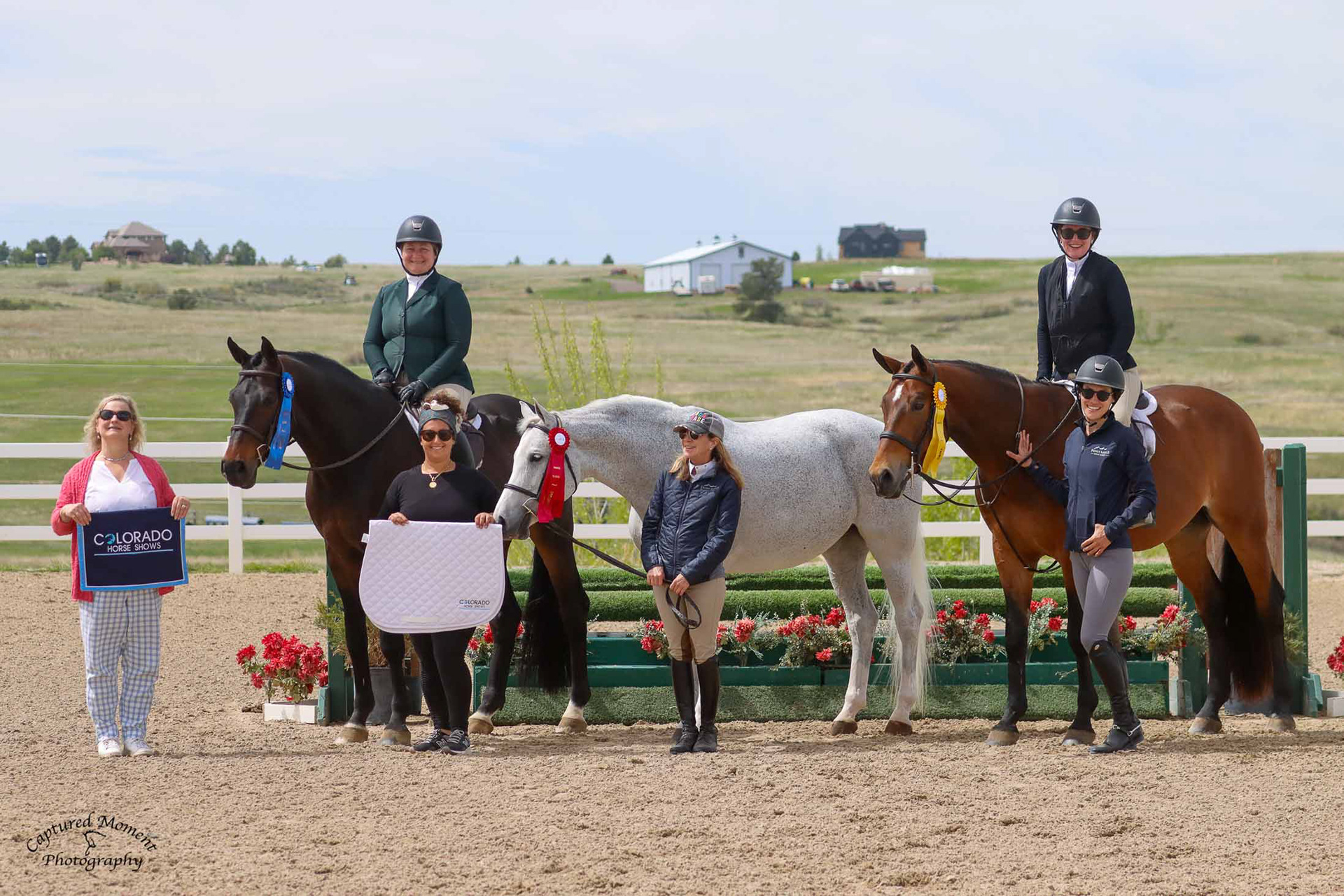 Group photo of riders and horses with ribbons in a show arena
