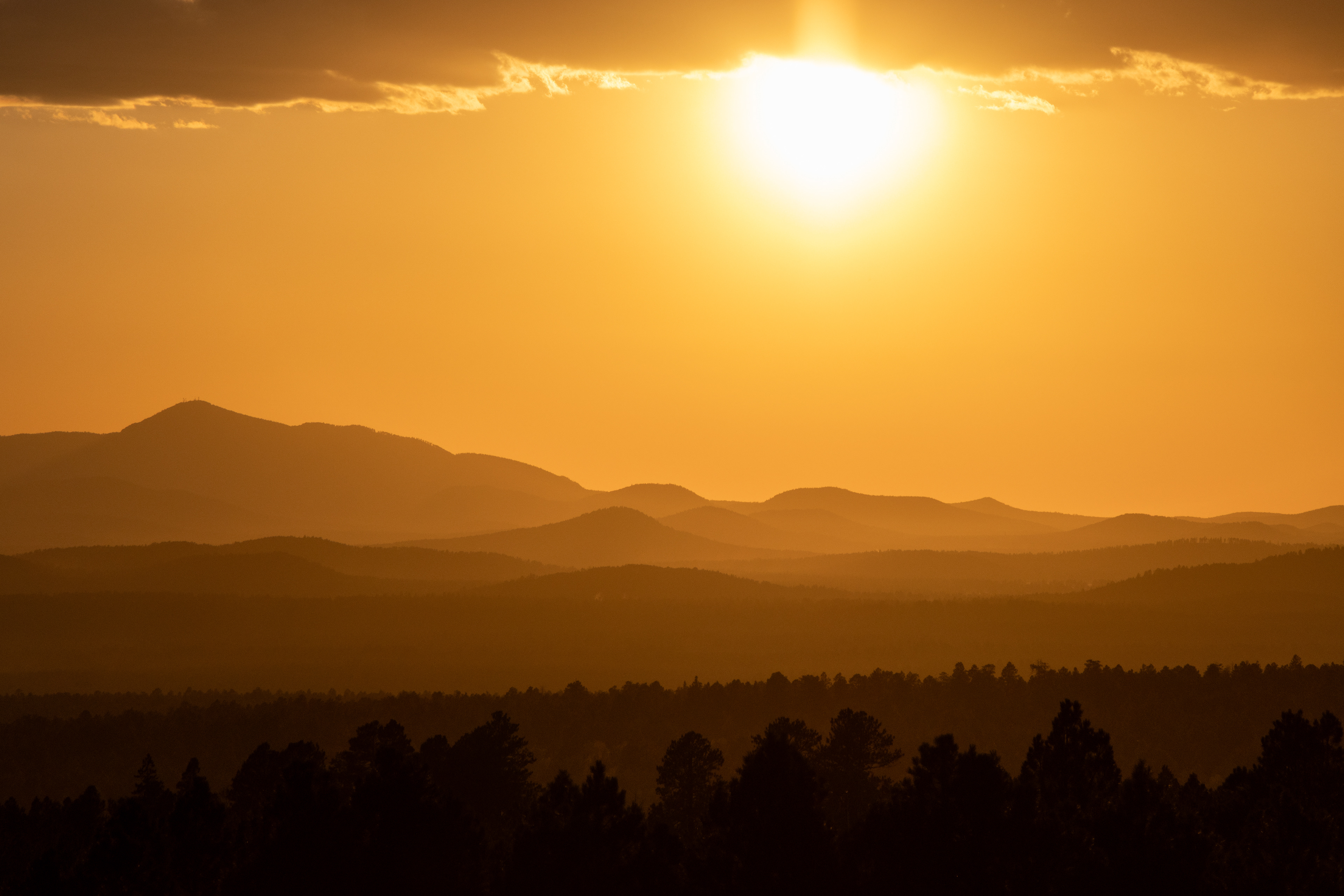 Golden sunset over mountain ridges and a forested horizon