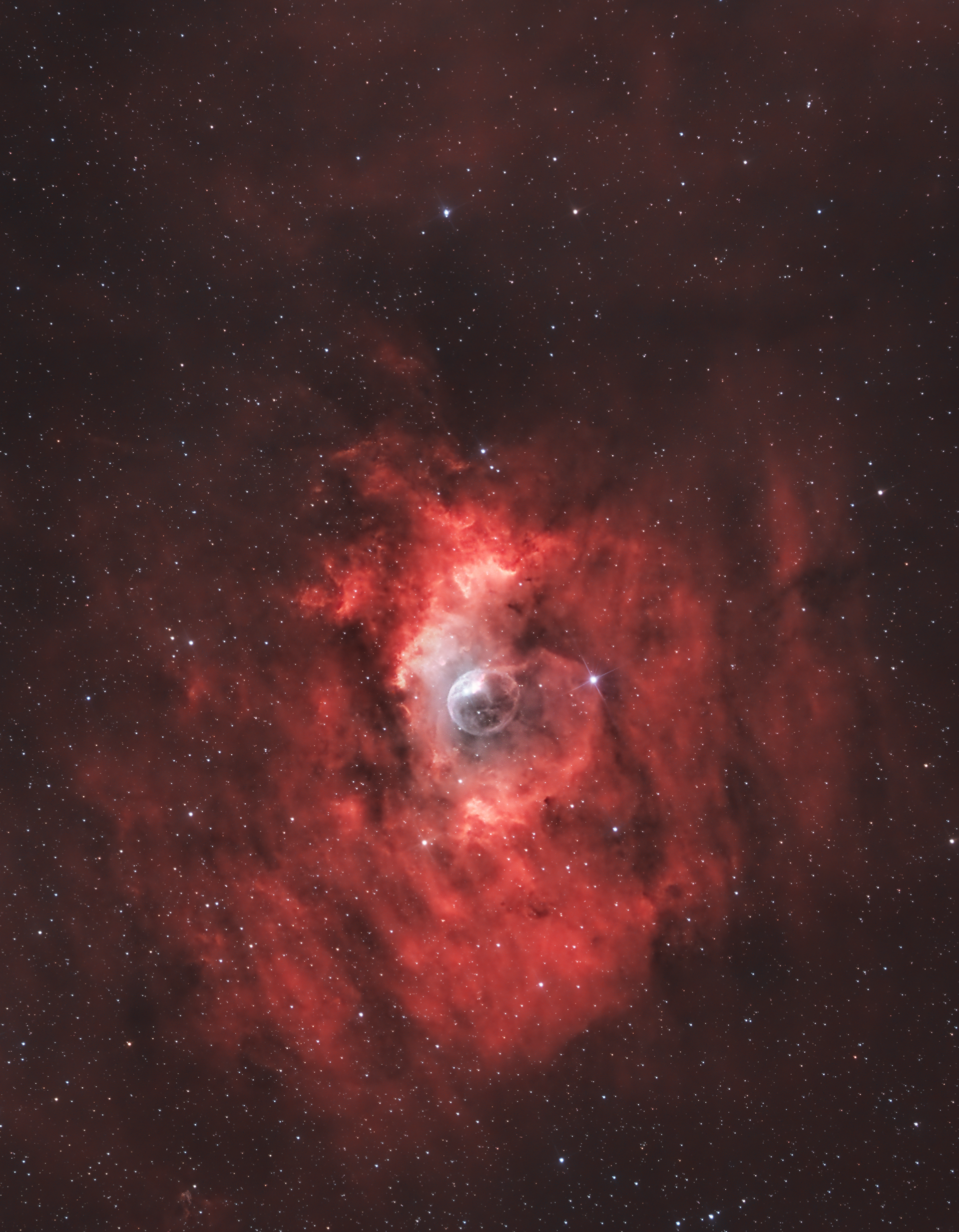The Bubble Nebula, also known as NGC 7635, is a stunning emission nebula located about 7,100 light-years away in the constellation Cassiopeia. It owes its name to the nearly spherical, bubble-like structure created by the powerful stellar winds of a massive, hot O-type star (SAO 20575) at its center. The nebula is roughly 10 light-years in diameter, with its vibrant hues resulting from ionized gases, primarily hydrogen, glowing under the influence of intense ultraviolet radiation. The Bubble Nebula is a captivating example of the dynamic interactions between stars and their surrounding interstellar environments.