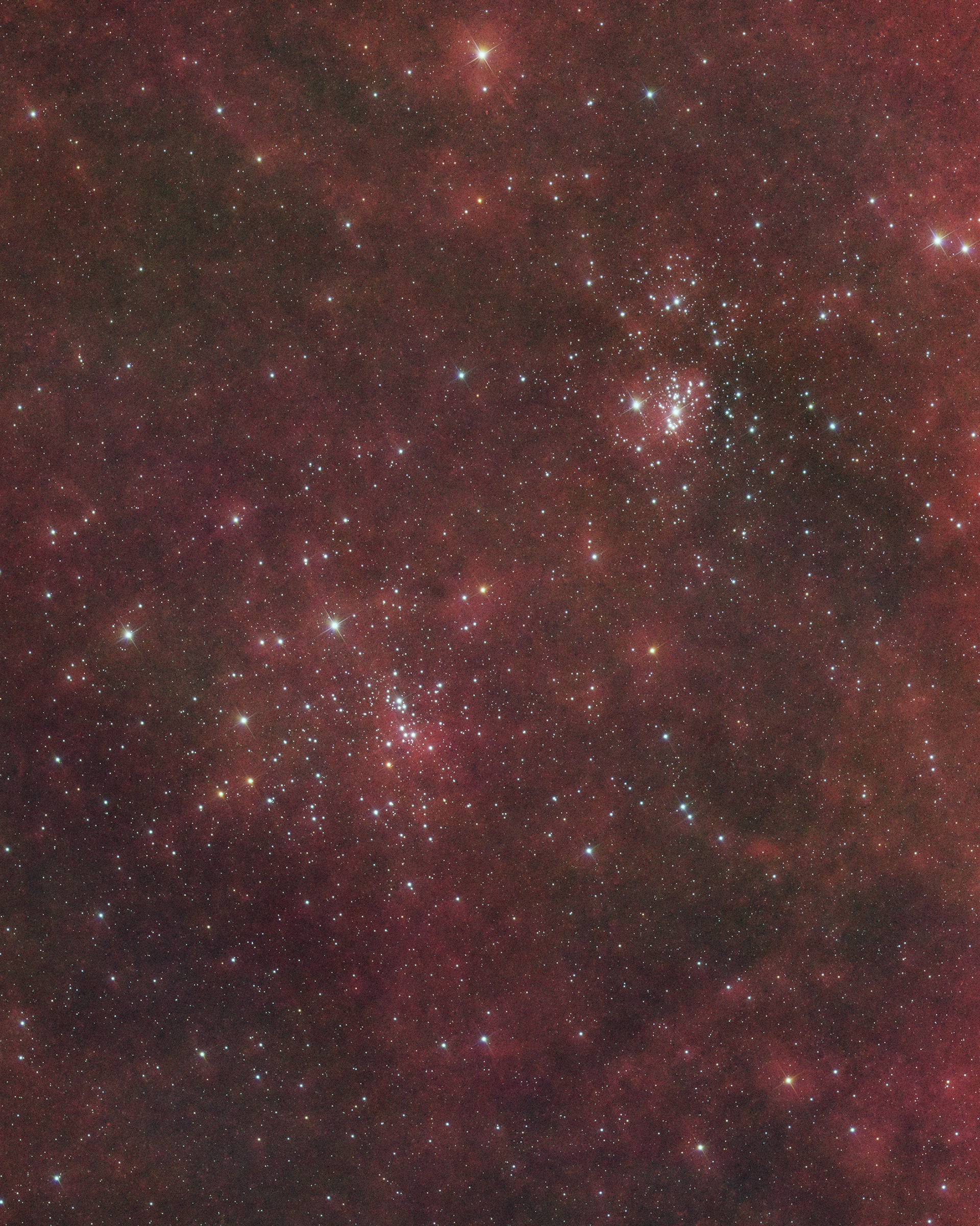 The Perseus Double Cluster, comprising NGC 869 and NGC 884, is a stunning pair of open star clusters about 7,500 light-years away in the constellation Perseus. These young clusters, around 12.8 million years old, feature bright blue stars and a few red supergiants, offering a vibrant celestial display. Surrounding the clusters are Hydrogen-alpha (Hα) clouds, which emit a soft, reddish glow, adding depth to the scene and highlighting the ionized hydrogen gas in this star-forming region of the Milky Way Galaxy.