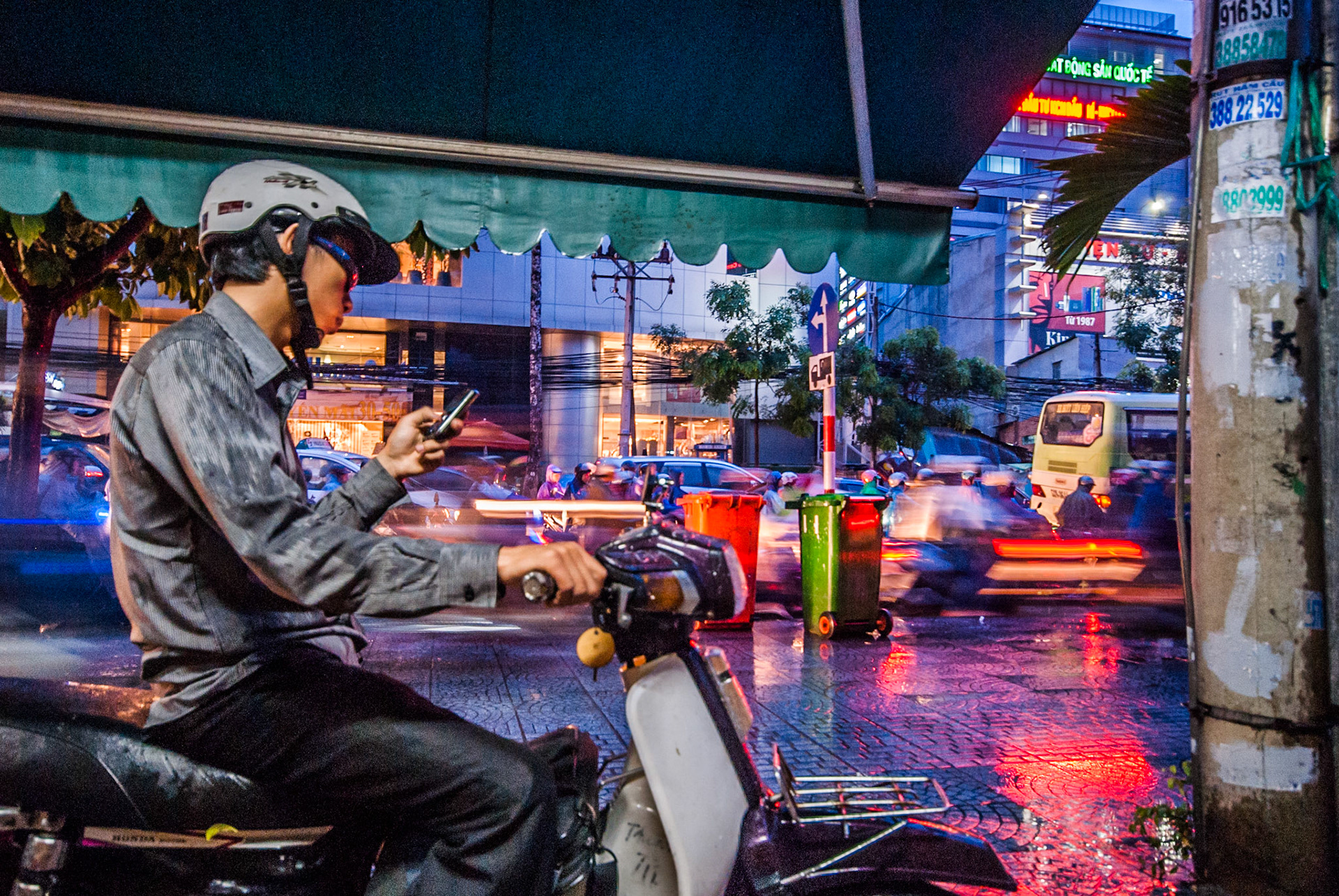 The afternoon monsoon rains hit downtown Ho Chi Minh City at rush hour. A thousand bikes seamed to appear from no where and flood the roads with metal and rubber as well as the rainwater. The road soon had no more space to offer the commuters and office workers, and the pavements became the new over-taking lane. The only dry space left to shelter and observe this spectacle was a clased shop front window. The pavement in-front became a pit-stop for those bikers needing to apply make-shift raincoats and answer mobile phones.