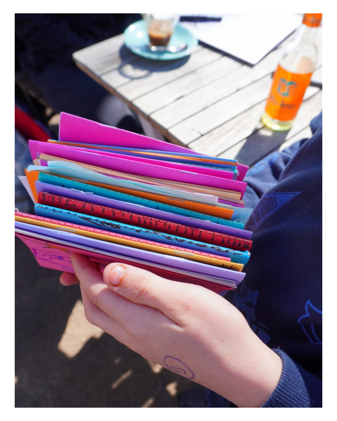 Ein Kind hält mehrere selbst gestaltete Reporter*innen-Hefte der Flippo-Kinderzeitung in die Kamera. Auf den bunten Covern: Namen, Zeichnungen und handgeschriebene Titel. Die Hefte entstanden in einem Schulworkshop mit der Flippo-Redaktion.