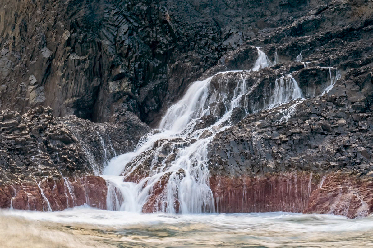 receding waves revealing the red skirted rocks