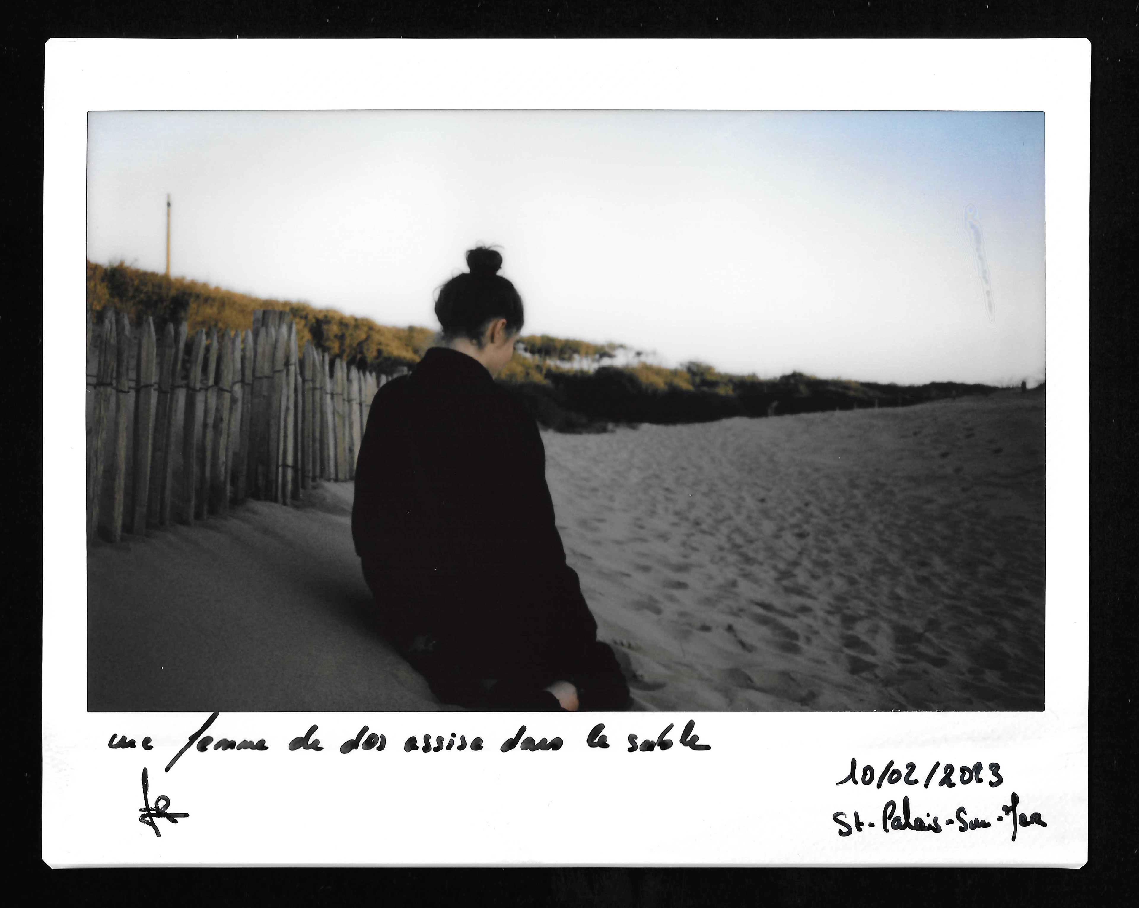 Une femme de dos assise dans le sable ©️